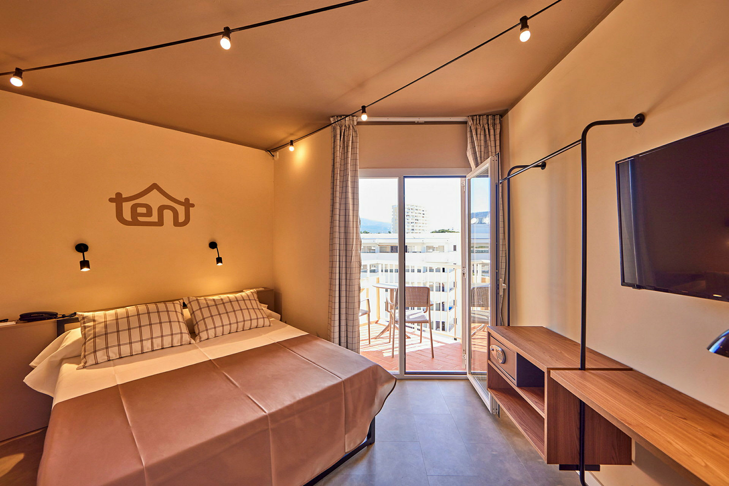 Ett hotellrum med en säng, väggdekoration, TV och en öppen balkongdörr. (AI-genererad text)