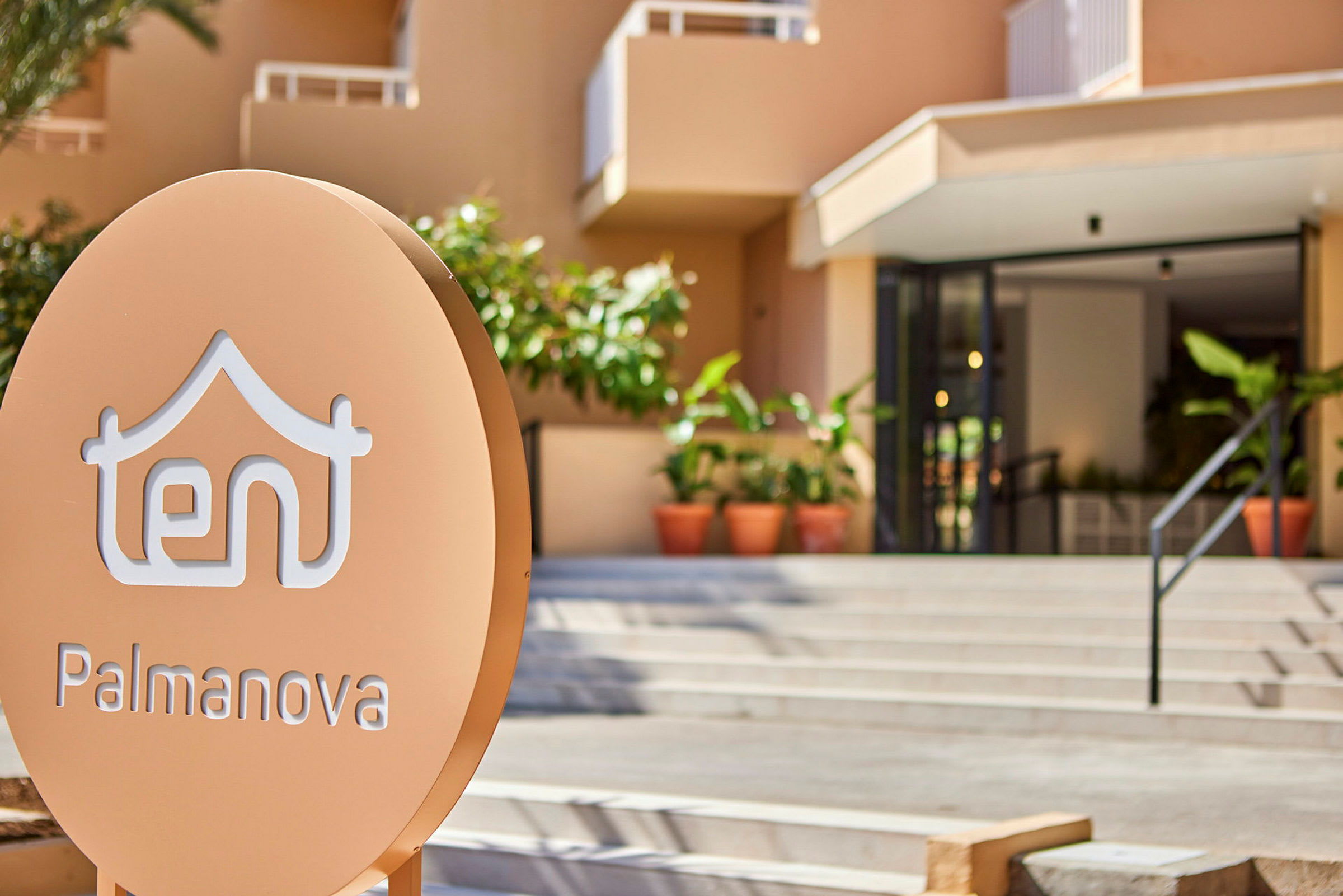 Skylt framför hotell TENT Palmanova med entré och växtlighet i bakgrunden. (AI-genererad text)