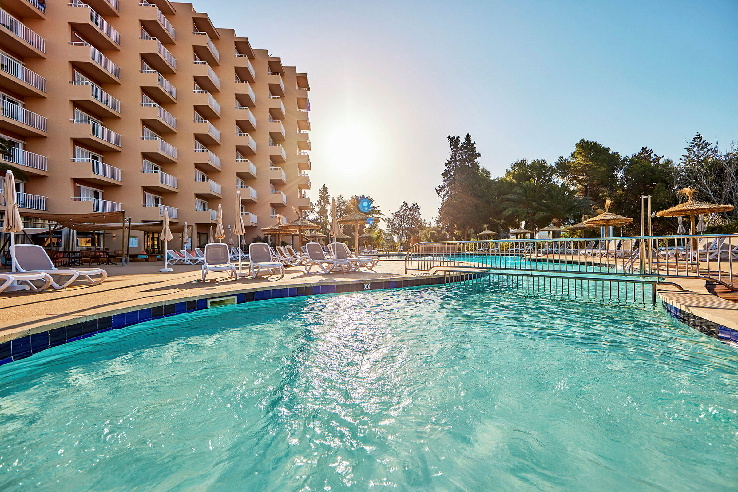 Bild av ett hotell med balkonger, en pool och solstolar på en solig dag. (AI-genererad text)