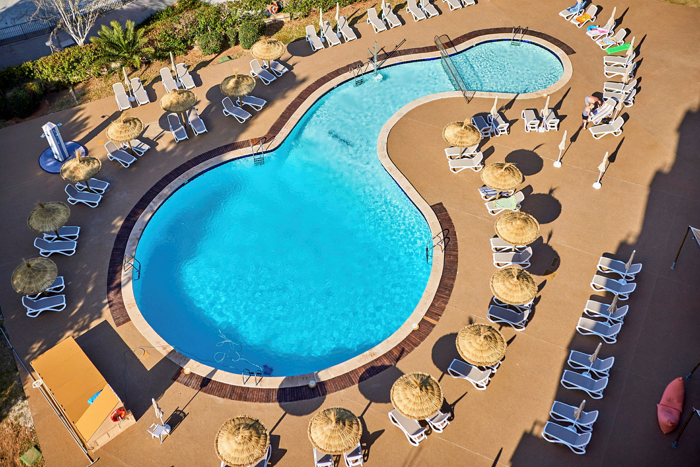 En swimmingpool omgiven av solstolar och parasoller. (AI-genererad text)