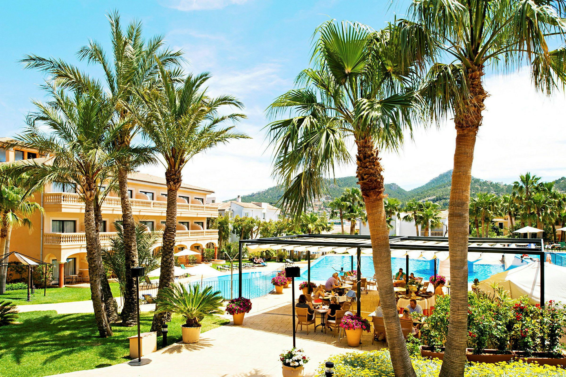 En hotellpool med solstolar och omgivande palmer samt en terrass med matplats. (AI-genererad text)