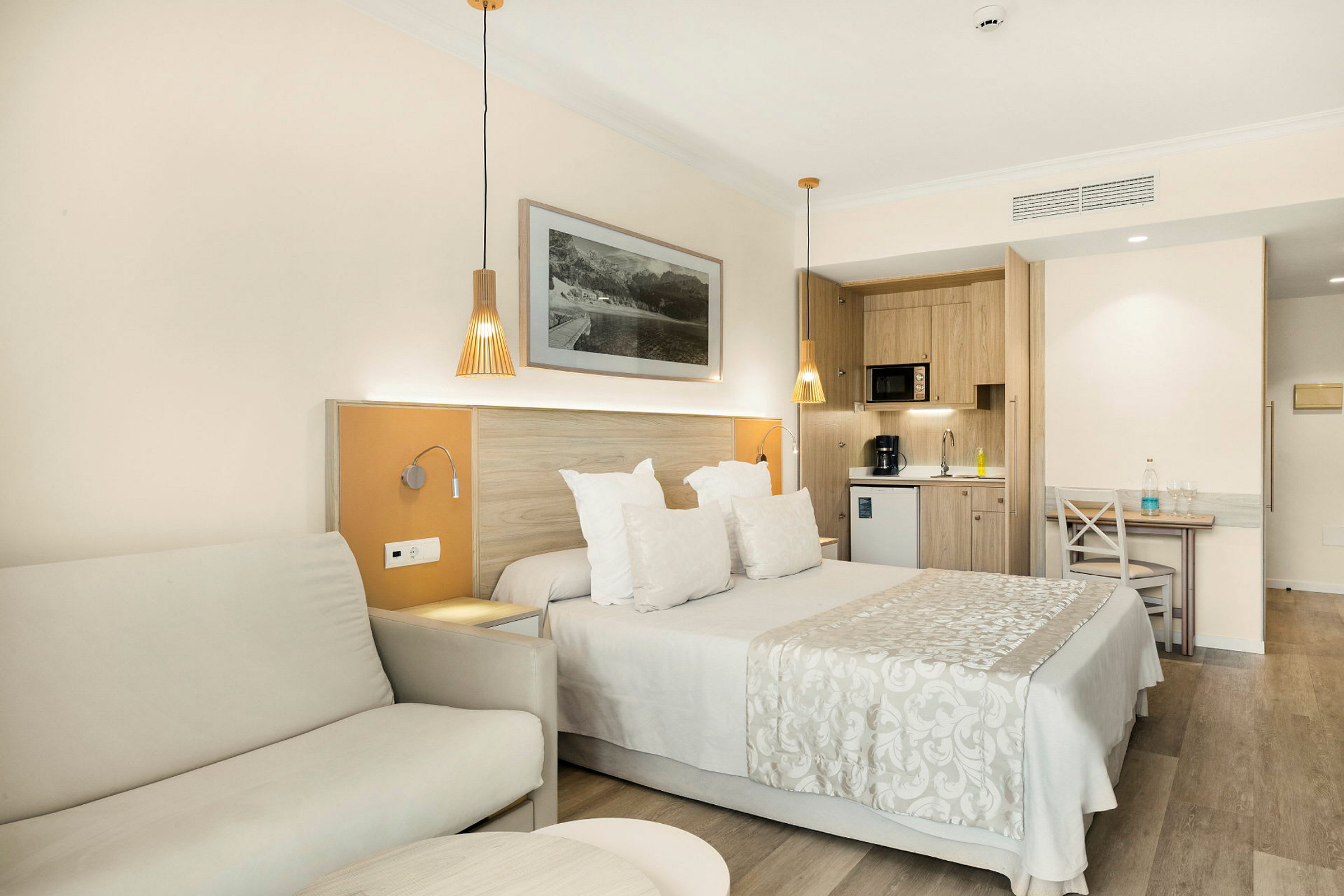 Ett hotellrum med en dubbelsäng, soffa och ett kök i bakgrunden. (AI-genererad text)