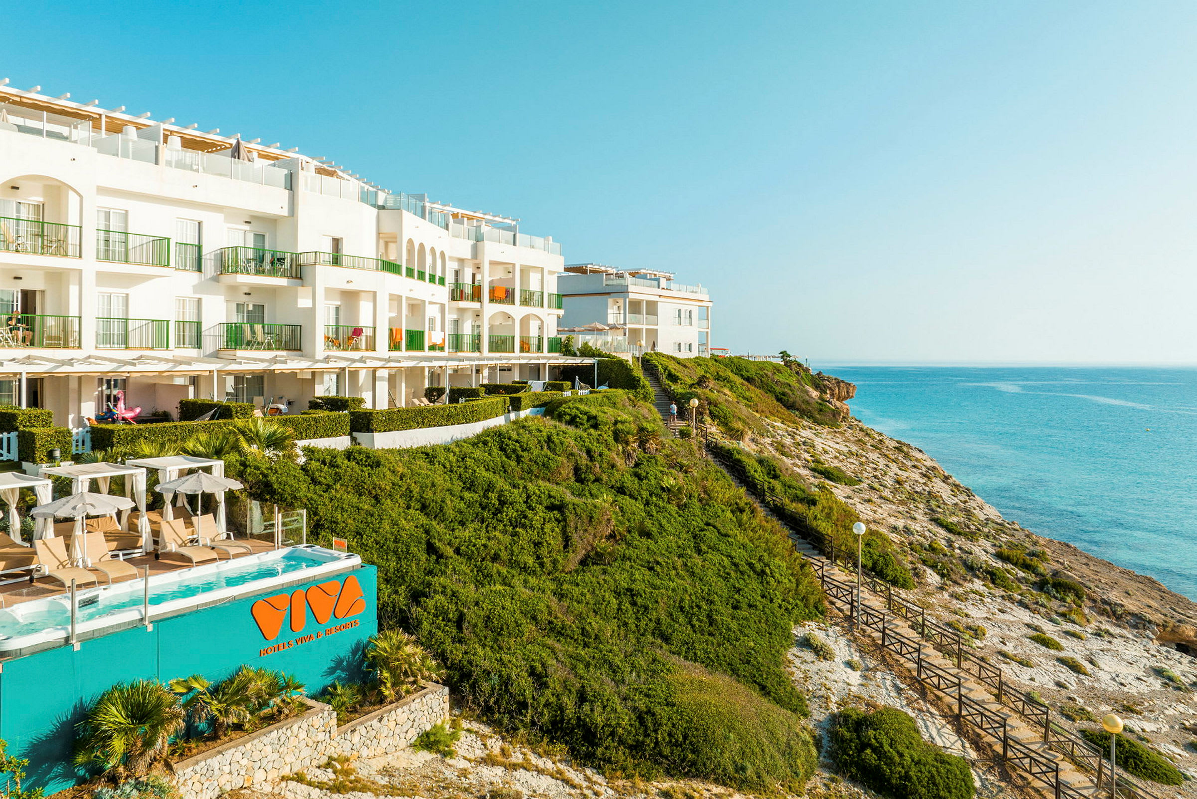 Ett hotell beläget på en klippa vid havet med pool och solstolar. (AI-genererad text)