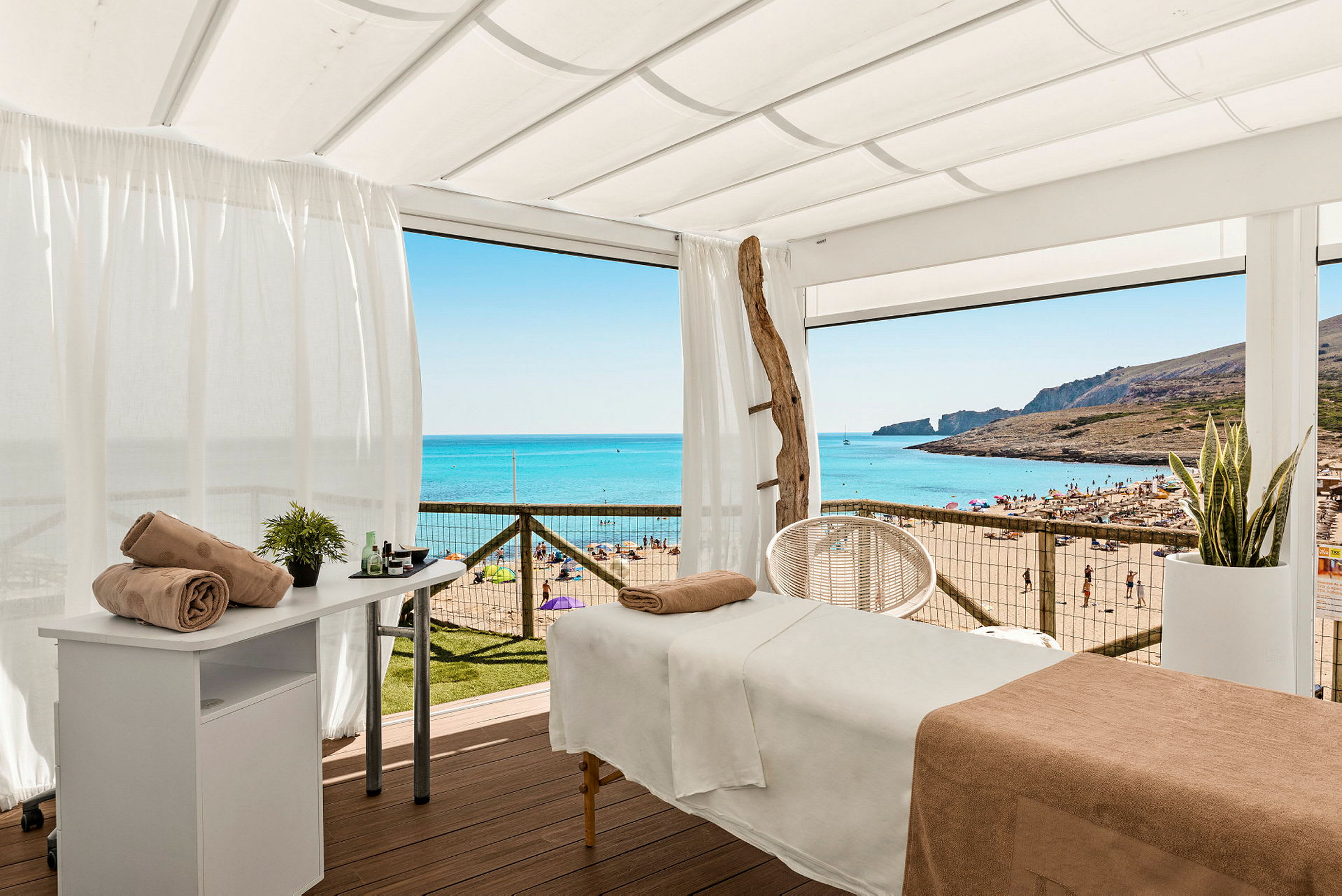 Massagebord under en vit skärm med utsikt över en solig strand. (AI-genererad text)