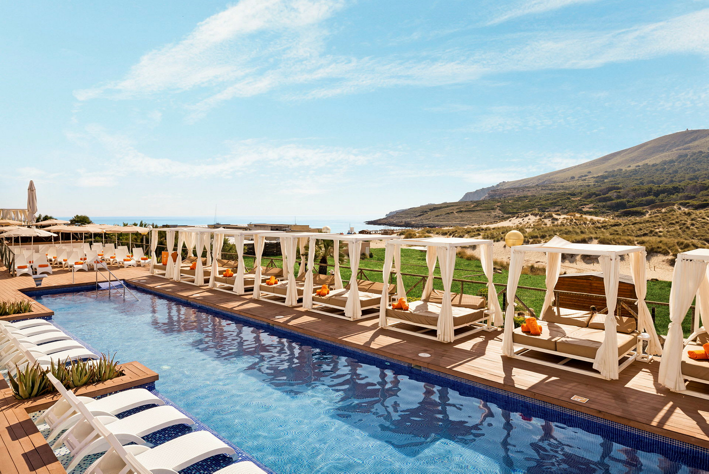 Dekorativa solstolar och skuggande sängar kring en modern pool på ett hotell nära stranden. (AI-genererad text)