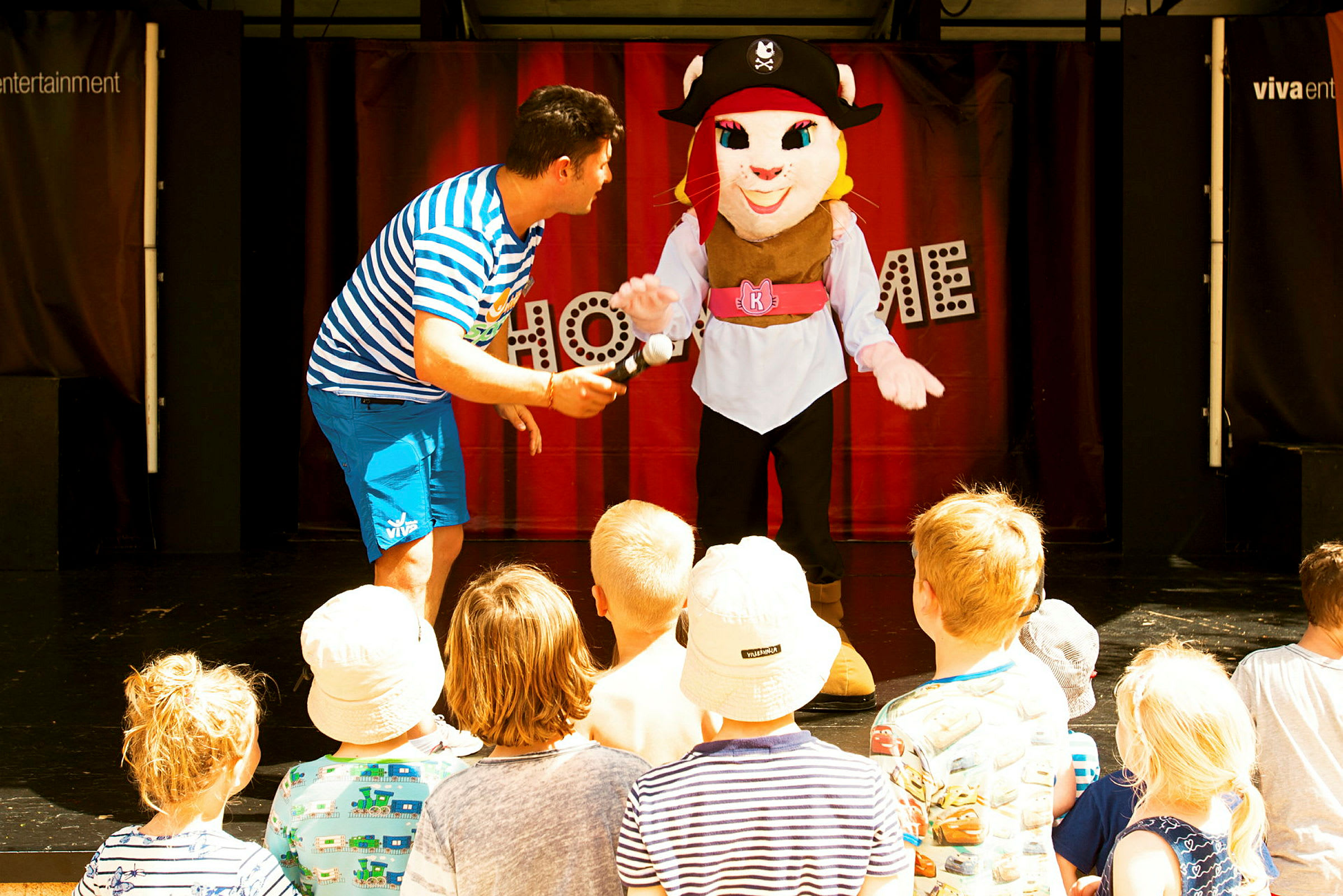 Scenföreställning med personer i kostym och publik av barn. (AI-genererad text)