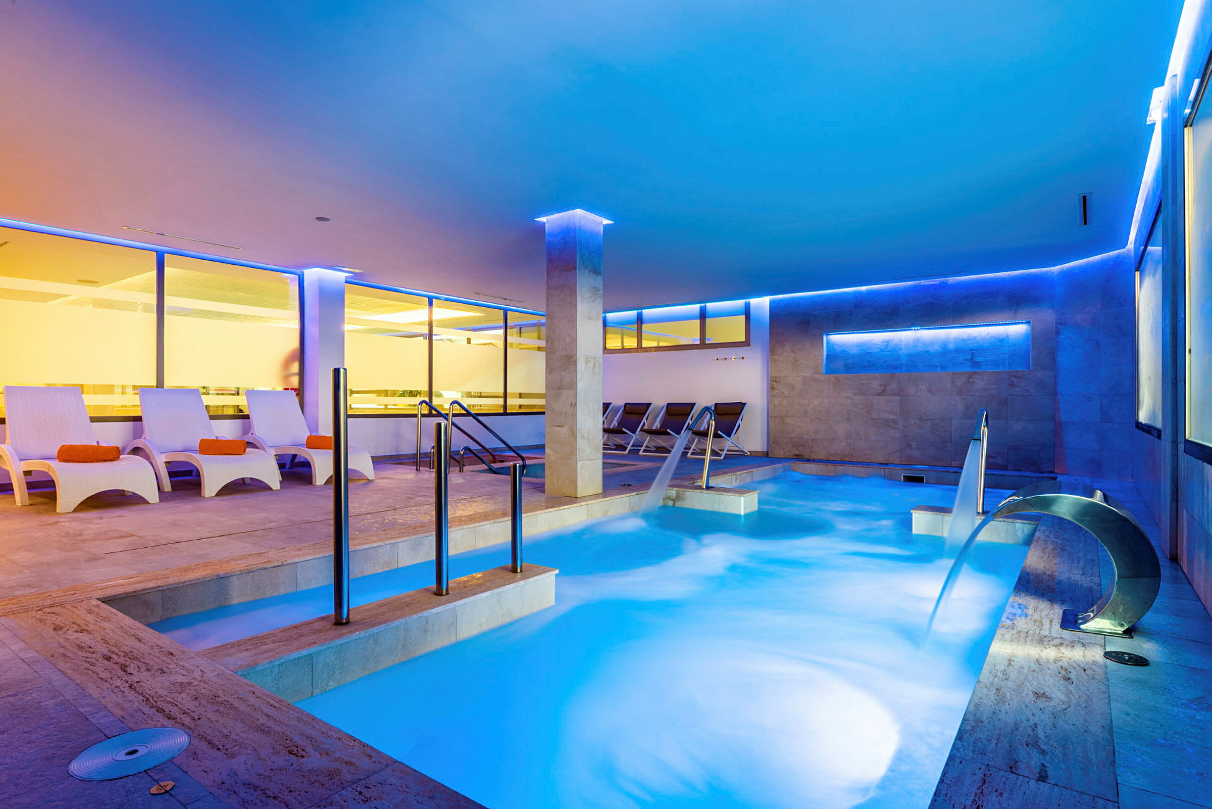 Inomhuspool med sittplatser och vattenkaskad i ett modern upplyst spa. (AI-genererad text)