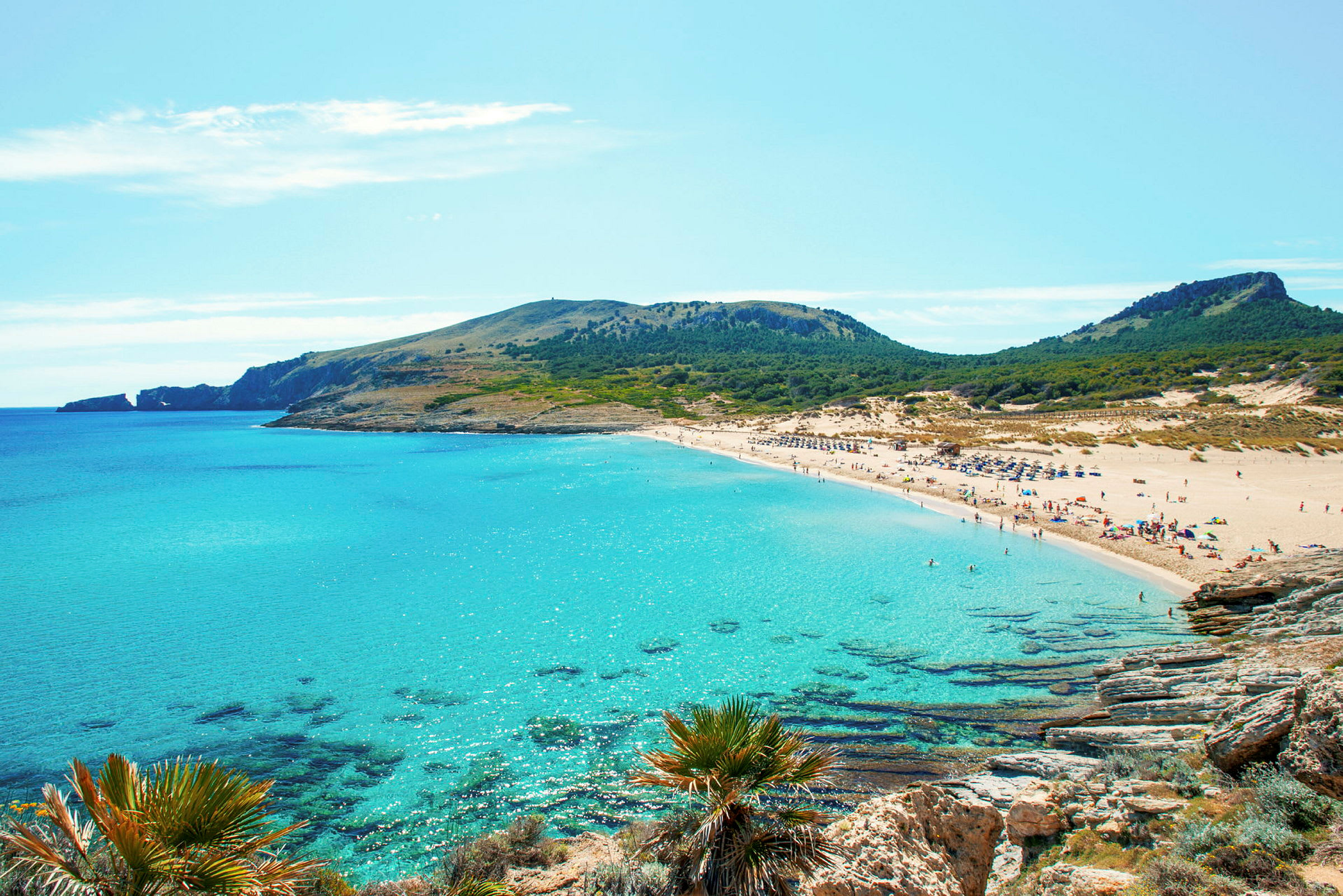En strand med klart turkost vatten, omgivet av klippor och grönska. (AI-genererad text)