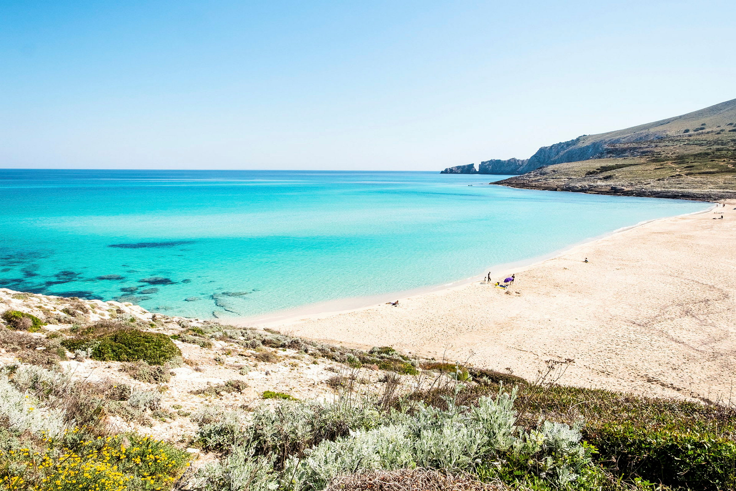 En strand med ljus sand och klarblått vatten, omgiven av grönska. (AI-genererad text)