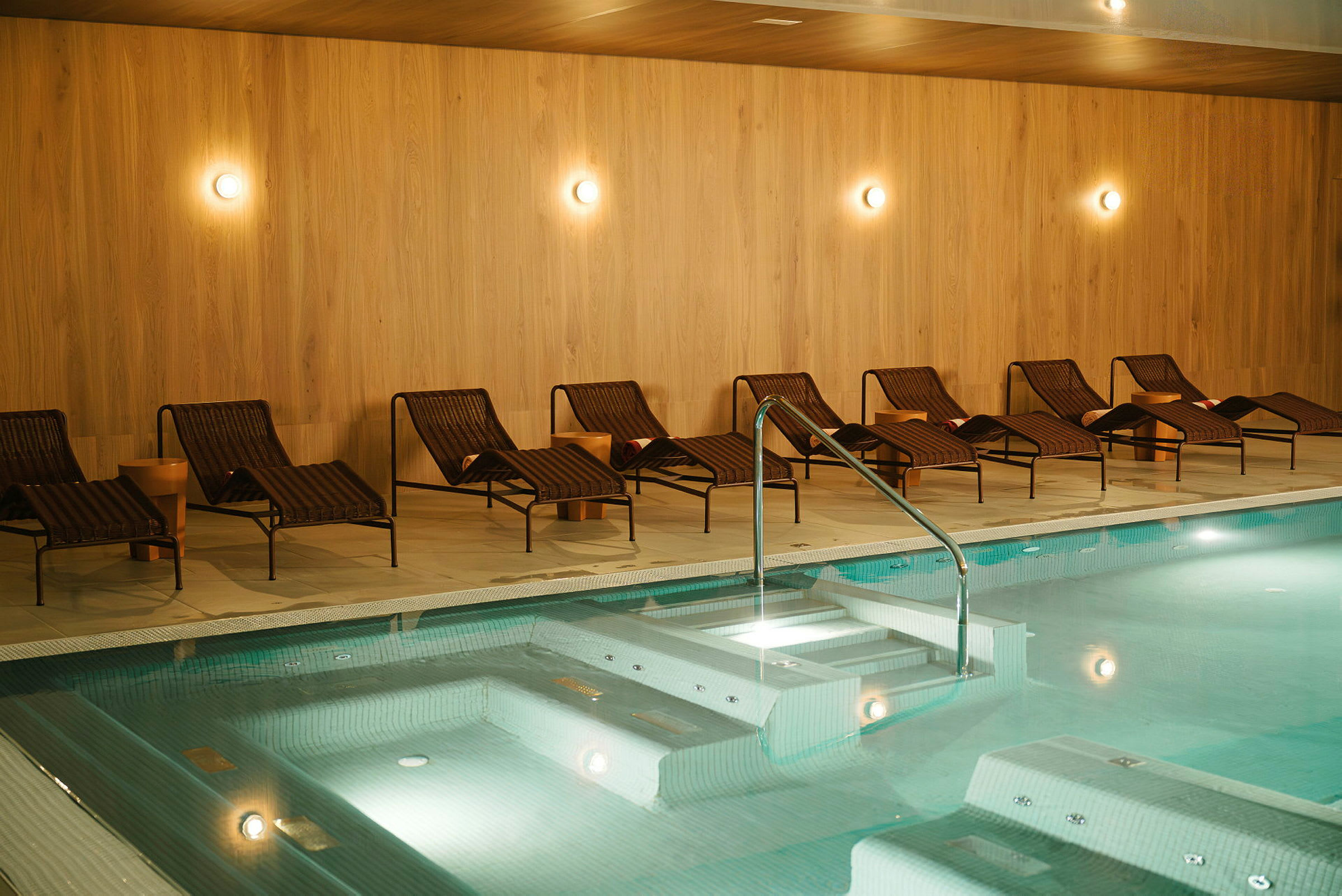Inomhuspool med solstolar och träpanelvägg. (AI-genererad text)