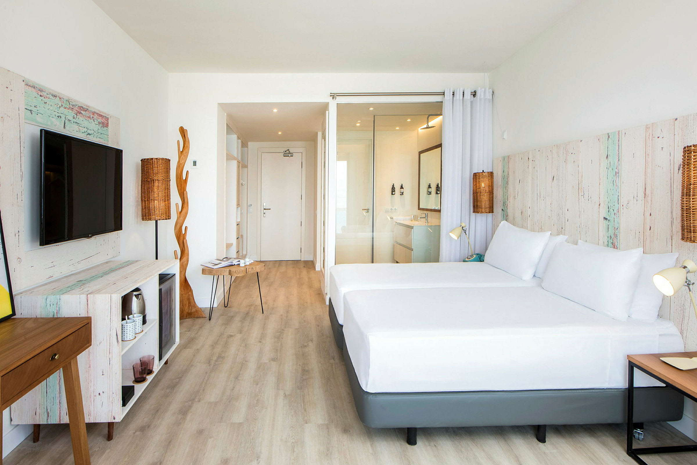 Ett ljust hotellrum med trädetaljer och moderna möbler. Rummet har en stor säng, en tv och en öppen planlösning. (AI-genererad text)
