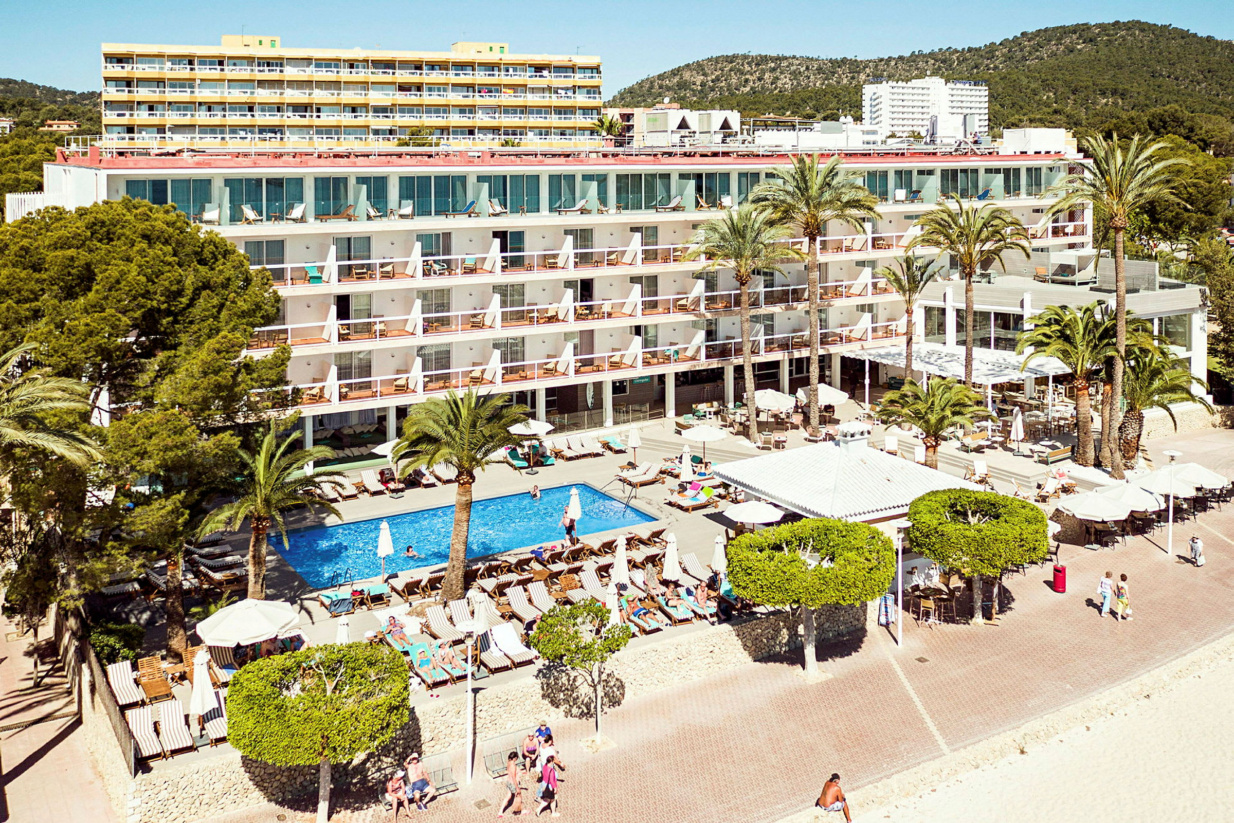 Ett hotell vid stranden med pool och solstolar omgivna av palmer. (AI-genererad text)
