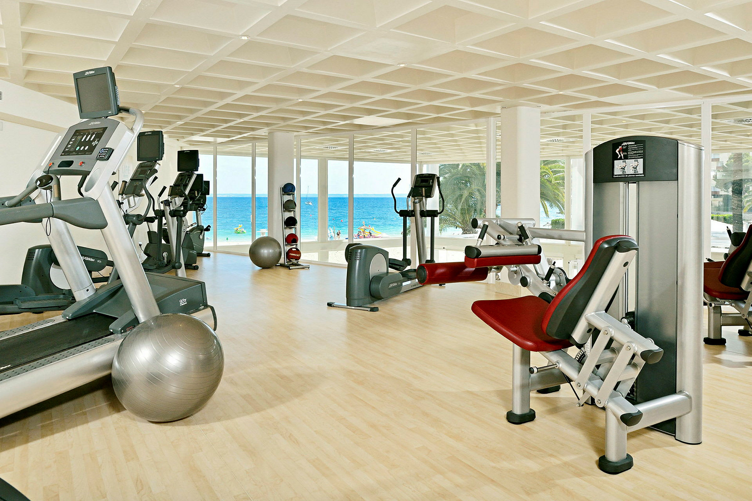 Ett gym med träningsutrustning och stora fönster som vetter mot stranden och havet. (AI-genererad text)