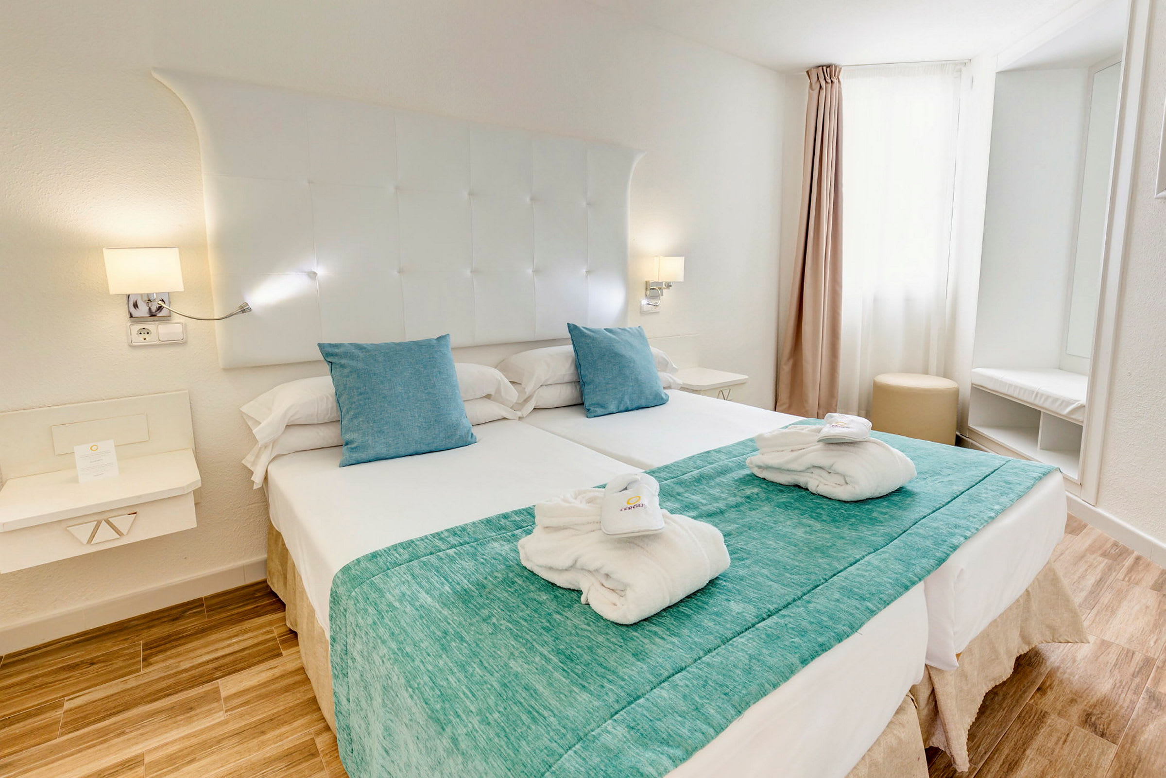 Ett hotellrum med dubbelsäng, vita lakan och ljusblå kuddar. (AI-genererad text)