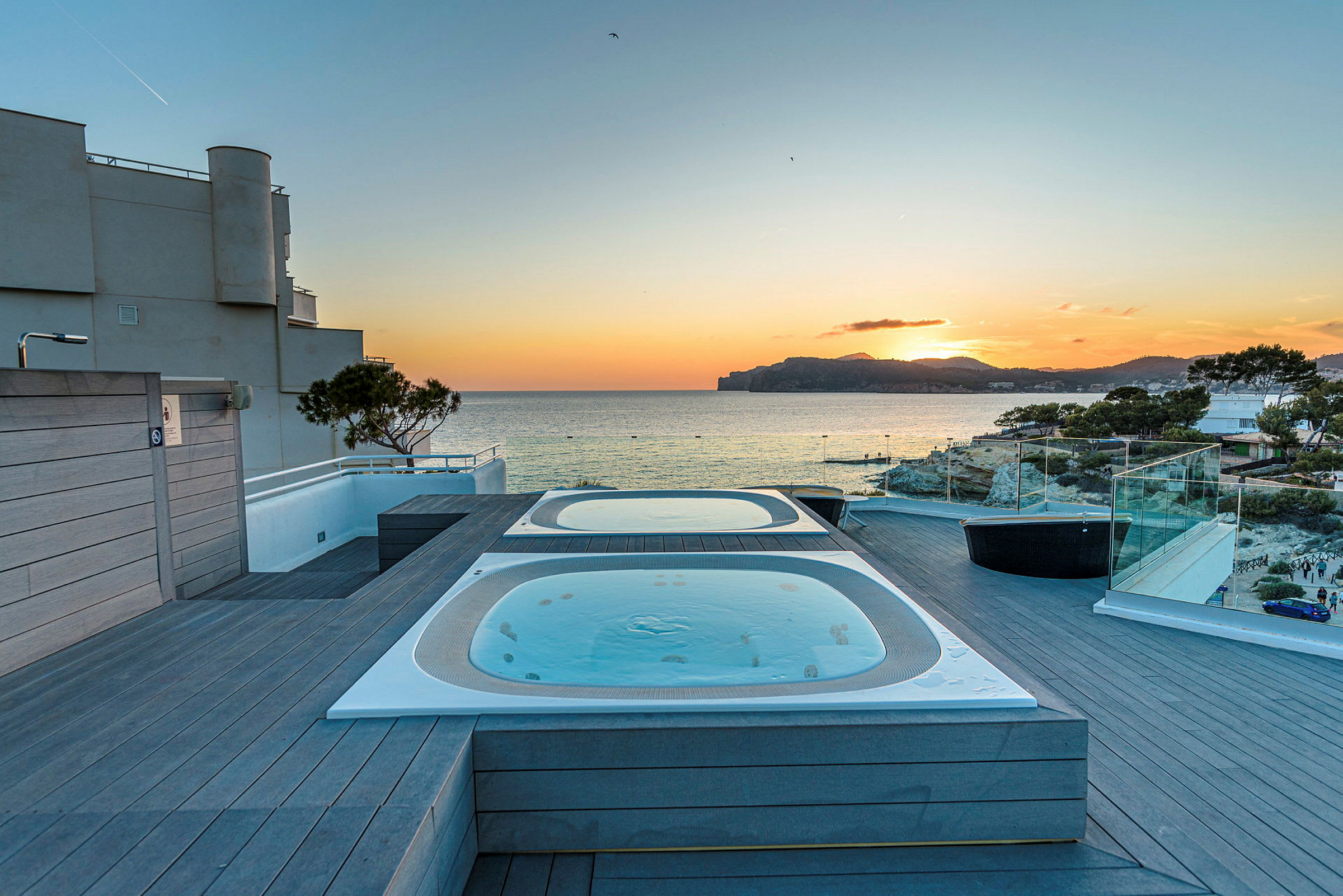 Två bubbelpooler på en terrass med utsikt över havet vid solnedgången. (AI-genererad text)