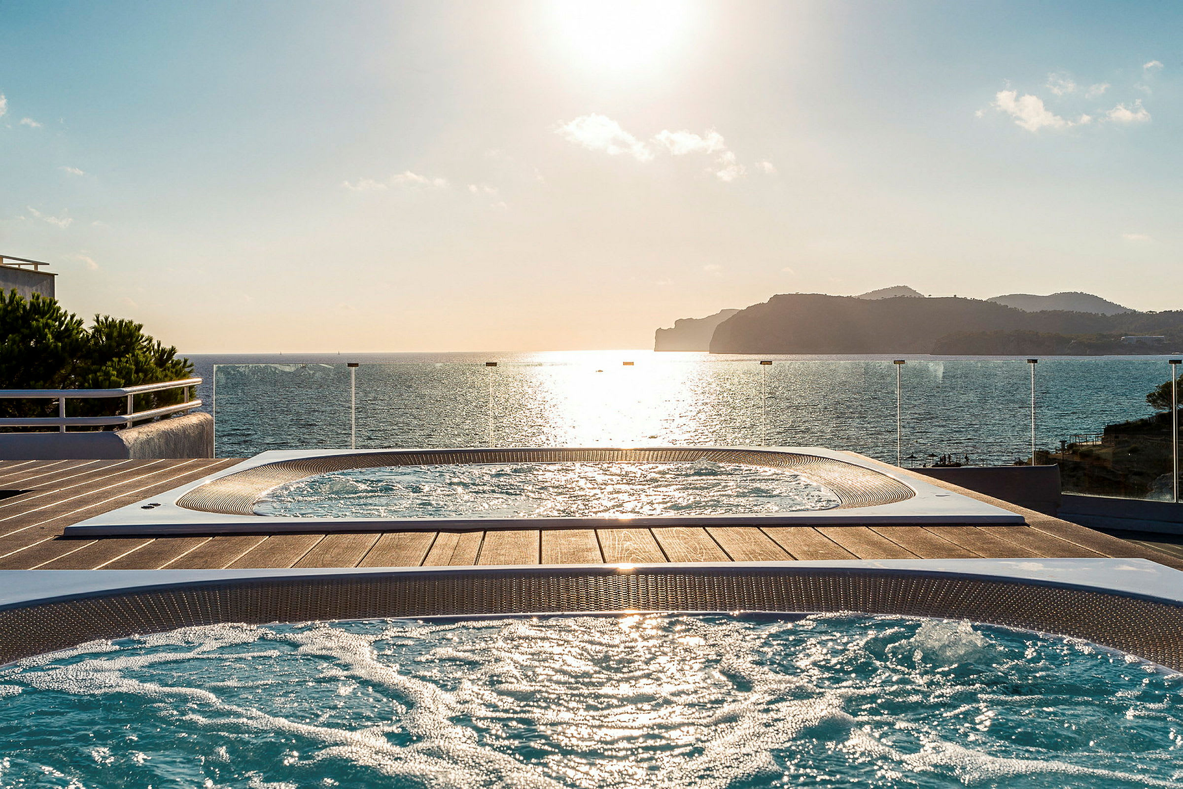 Två jacuzzi-bassänger på en terrass med utsikt över havet vid solnedgången. (AI-genererad text)