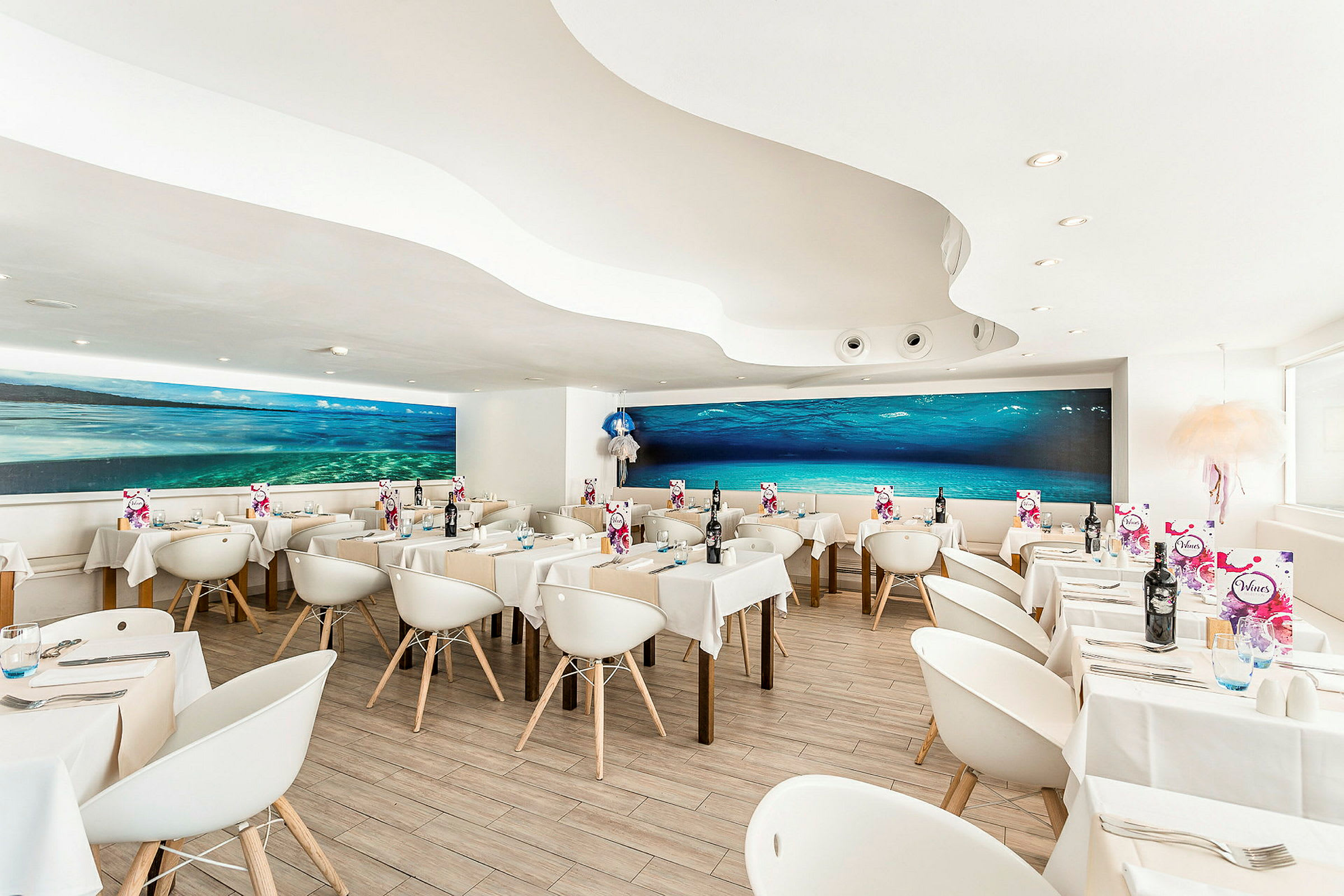 En modern restaurang med vita stolar och bord, samt en stor undervattensmålning på väggen. (AI-genererad text)