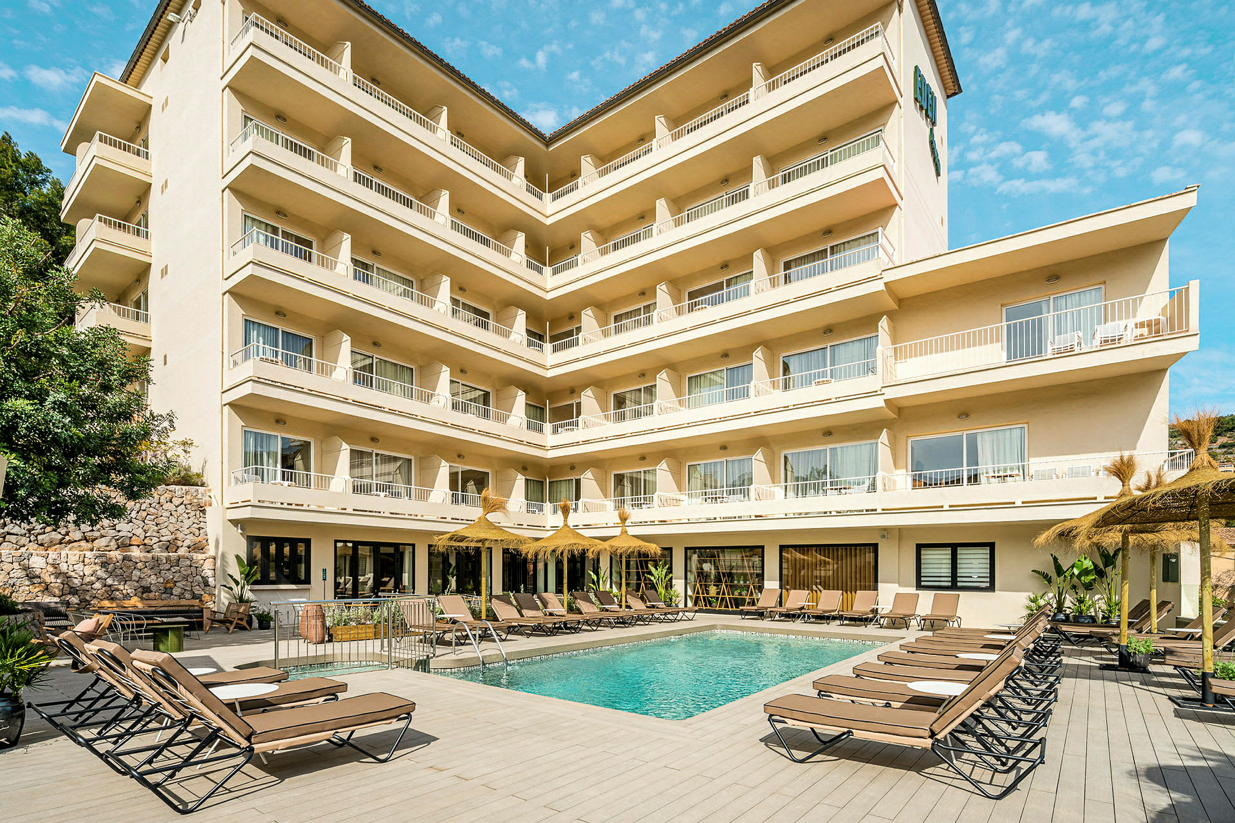 Hotellbyggnad med pool och solstolar i förgrunden. (AI-genererad text)