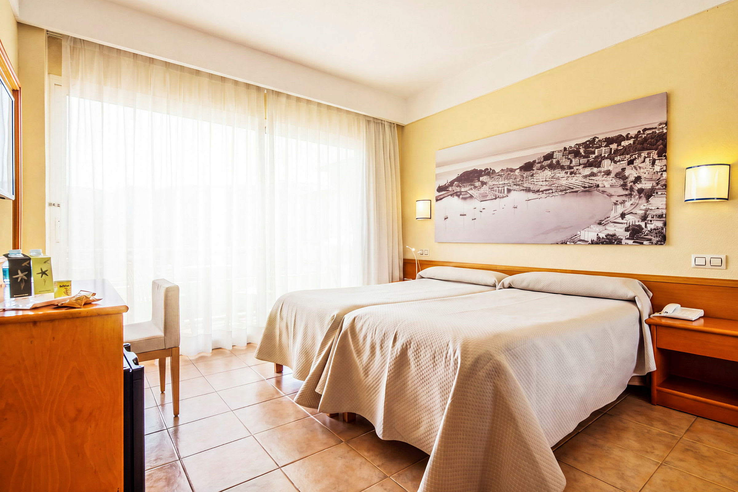 Ett hotellrum med två enkelsängar och en stor tavla på väggen. Rummet har ljusa gardiner och träinredning. (AI-genererad text)