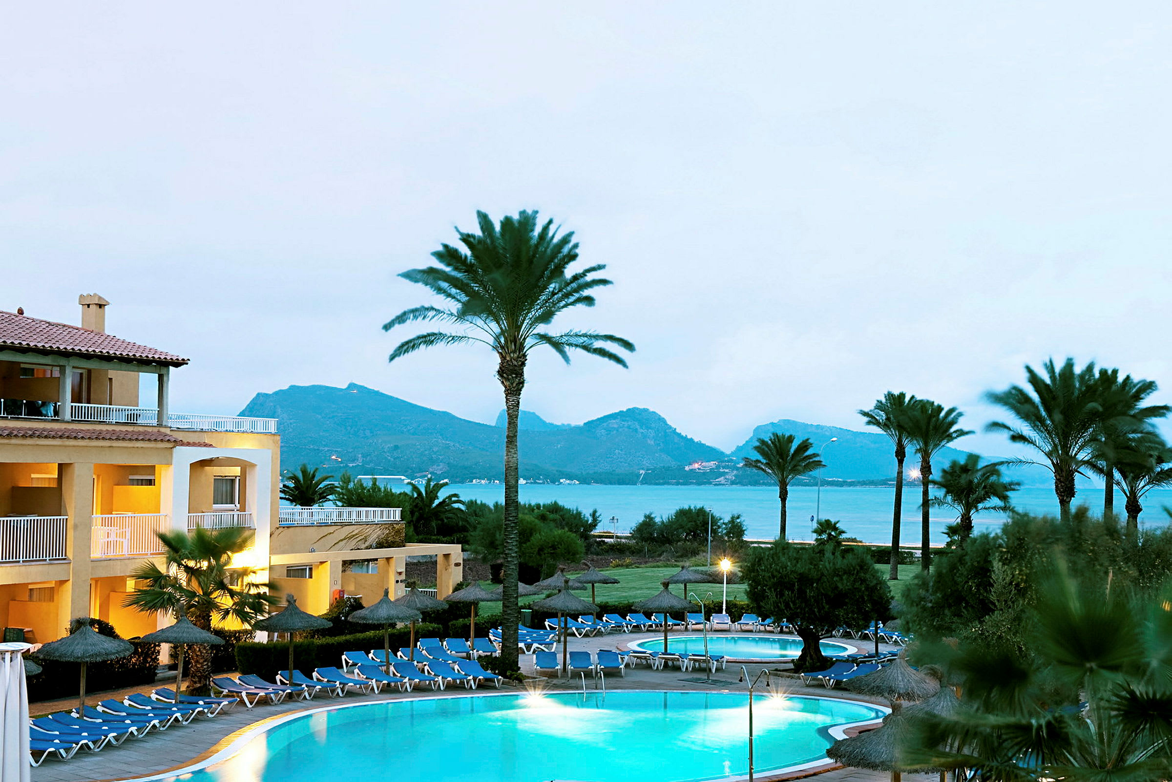 Hotell med pool, omgiven av palmer och sjöutsikt. (AI-genererad text)