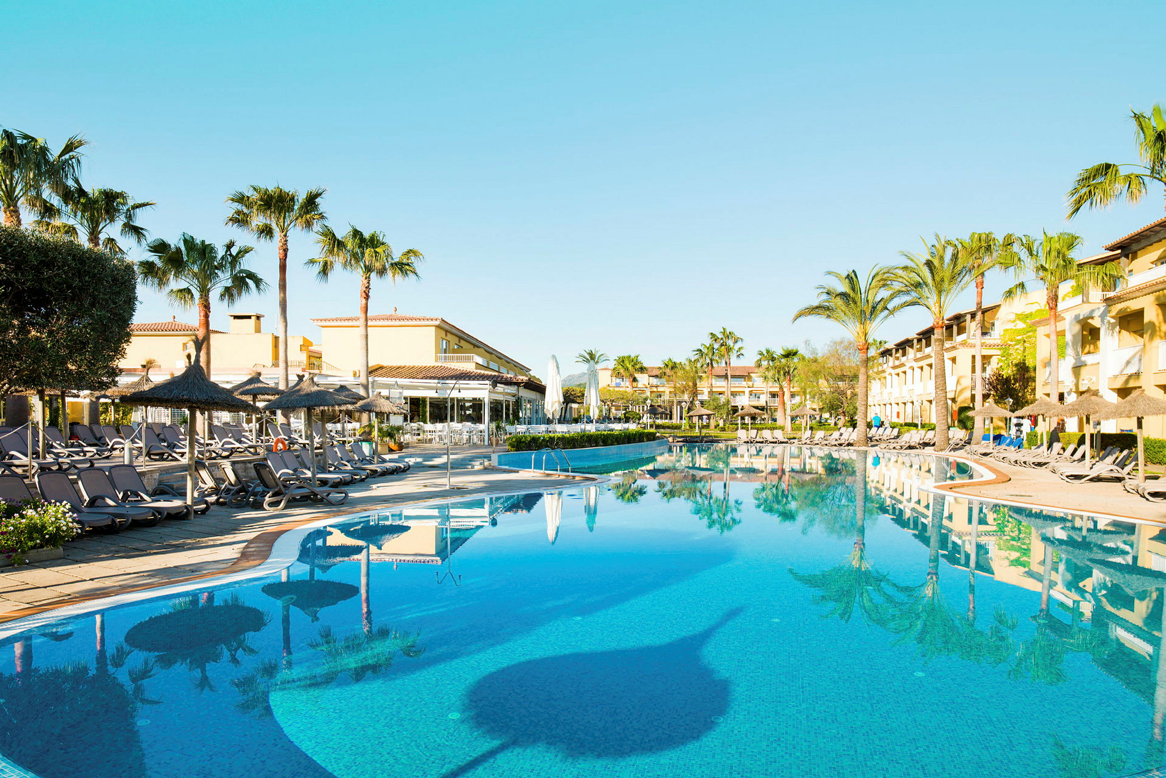 Poolområde med solstolar, palmer och hotellbyggnader. (AI-genererad text)