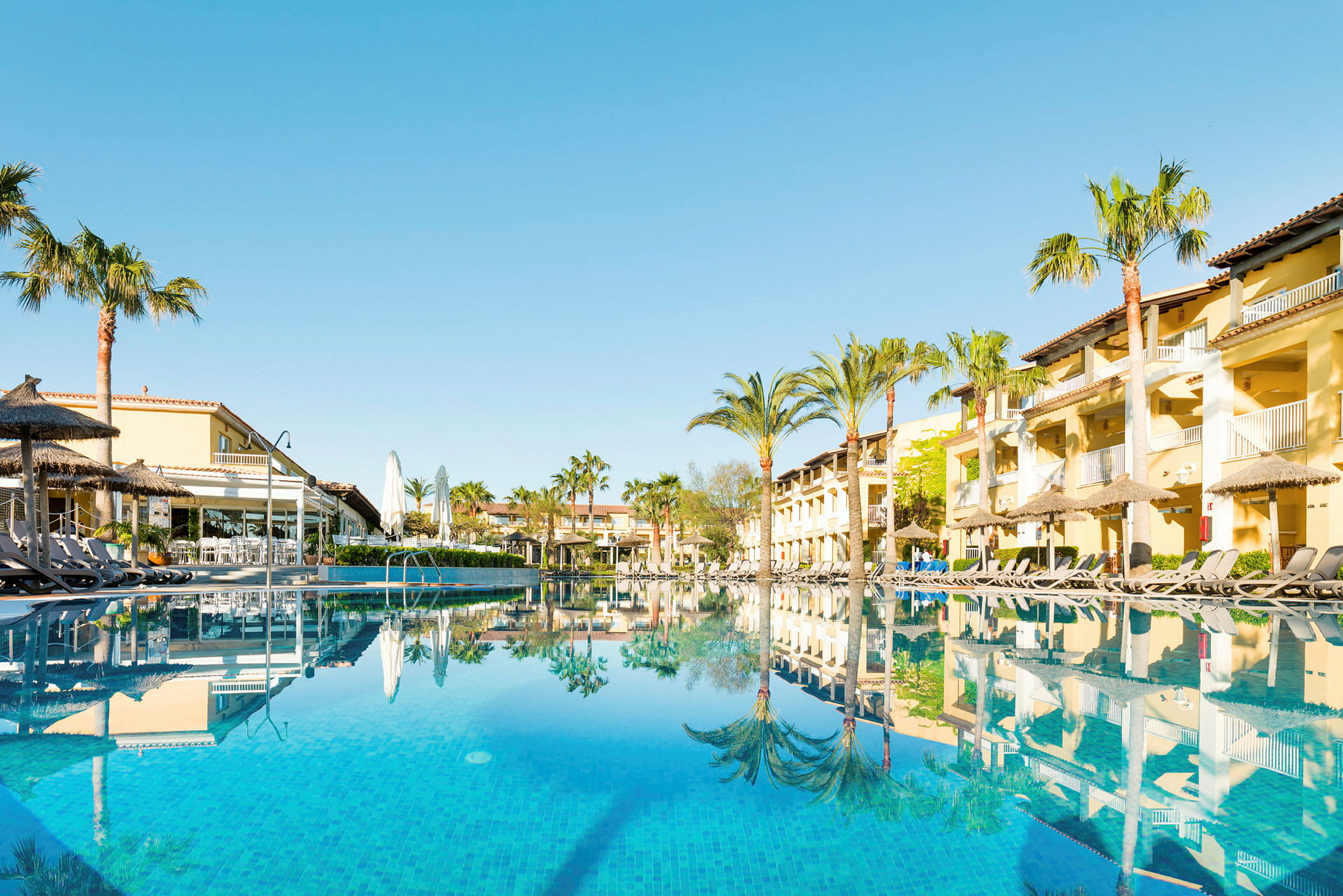 Hotellbyggnader och swimmingpool med solsängar vid poolkanten. (AI-genererad text)