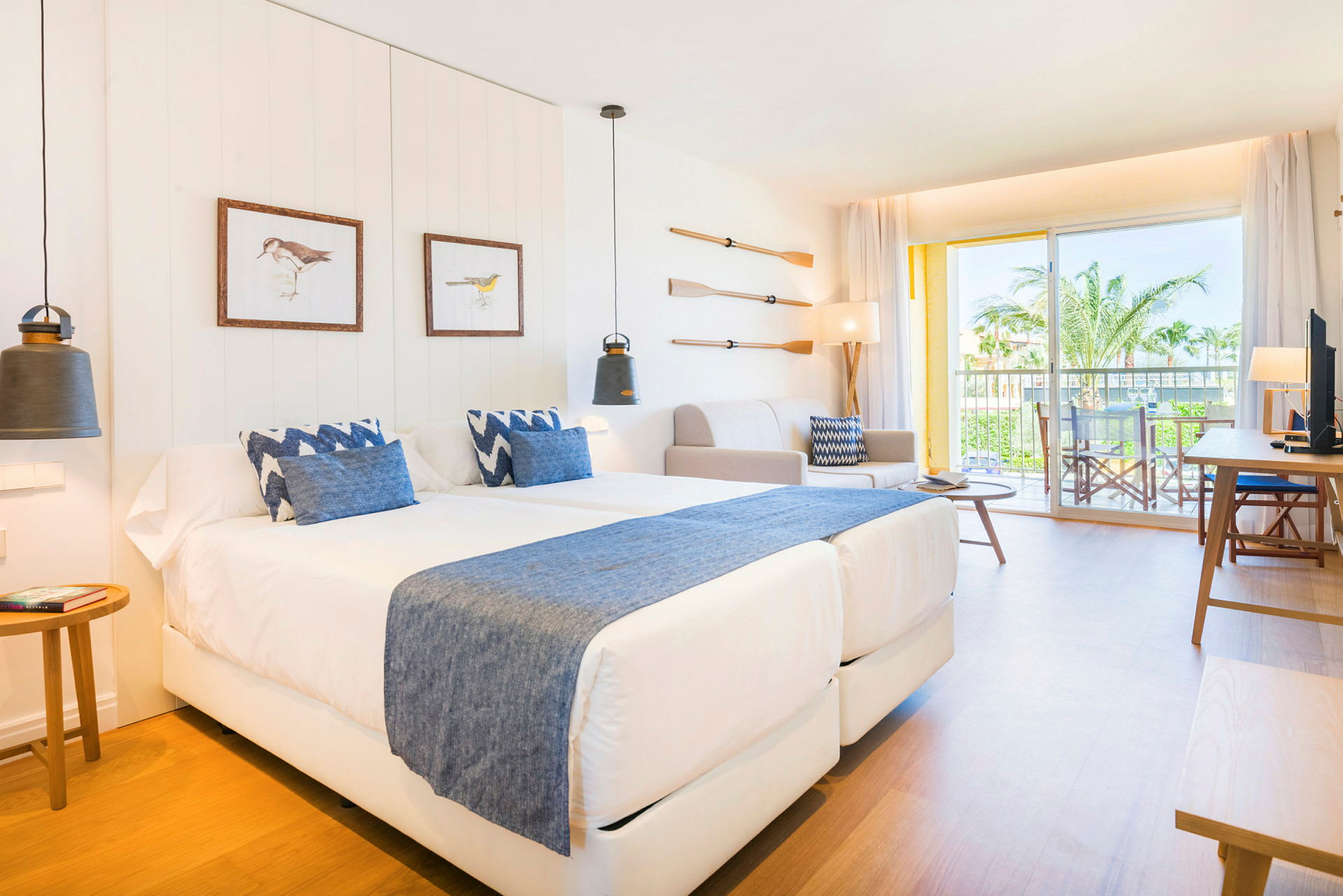 Ett modernt hotellrum med två sängar och blå detaljer samt en balkong med utsikt mot palmer. (AI-genererad text)