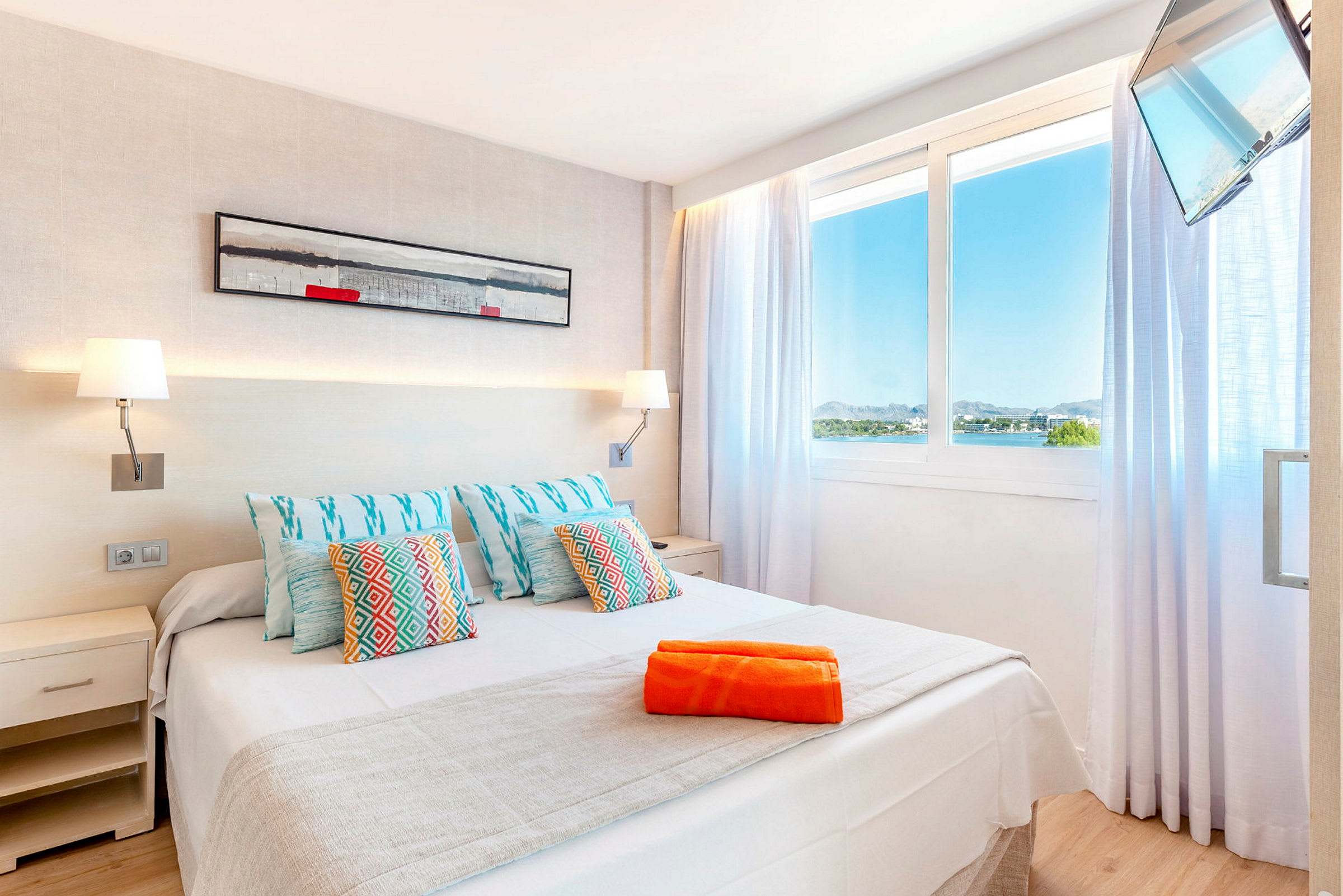 Hotellrum med upplyst väggdekor, stor säng och utsikt över landskap genom fönstret. (AI-genererad text)