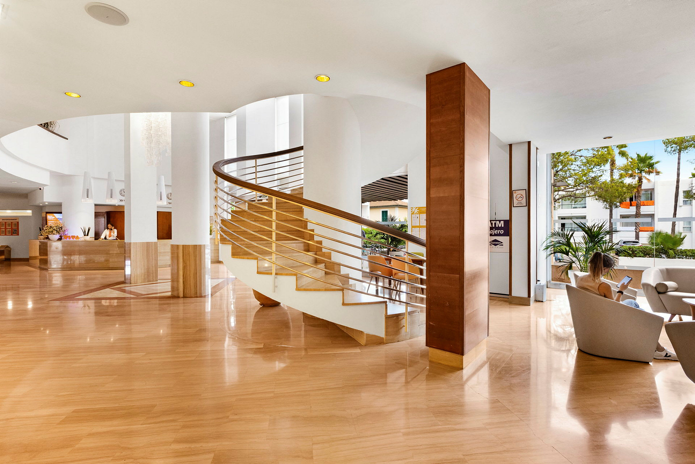 Ett ljust hotellobby med en spiraltrappa i centrum, receptionen till vänster och sittplatser till höger. (AI-genererad text)
