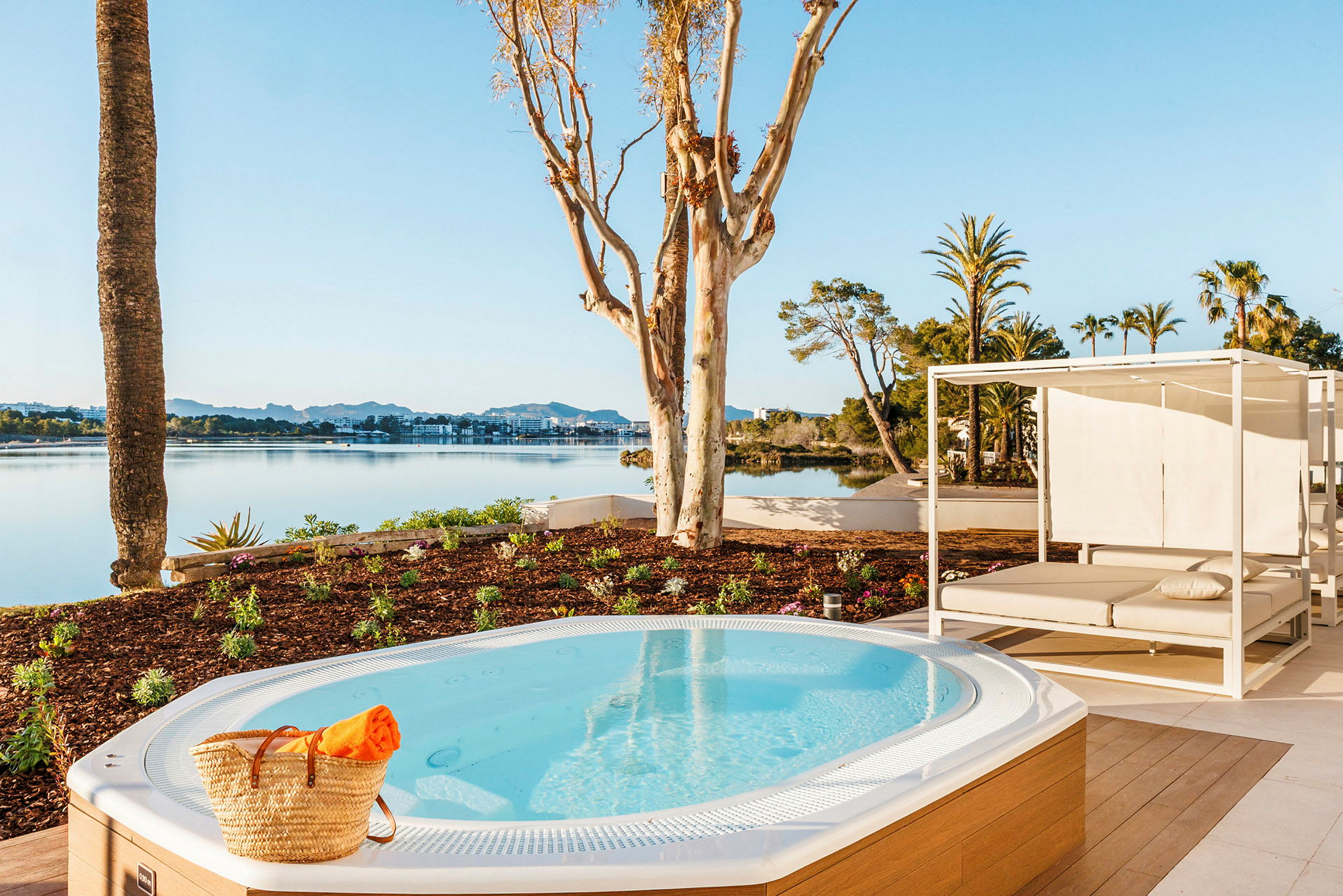 En jacuzzi med utsikt över en sjö, omgiven av trädgård och en solsäng. (AI-genererad text)