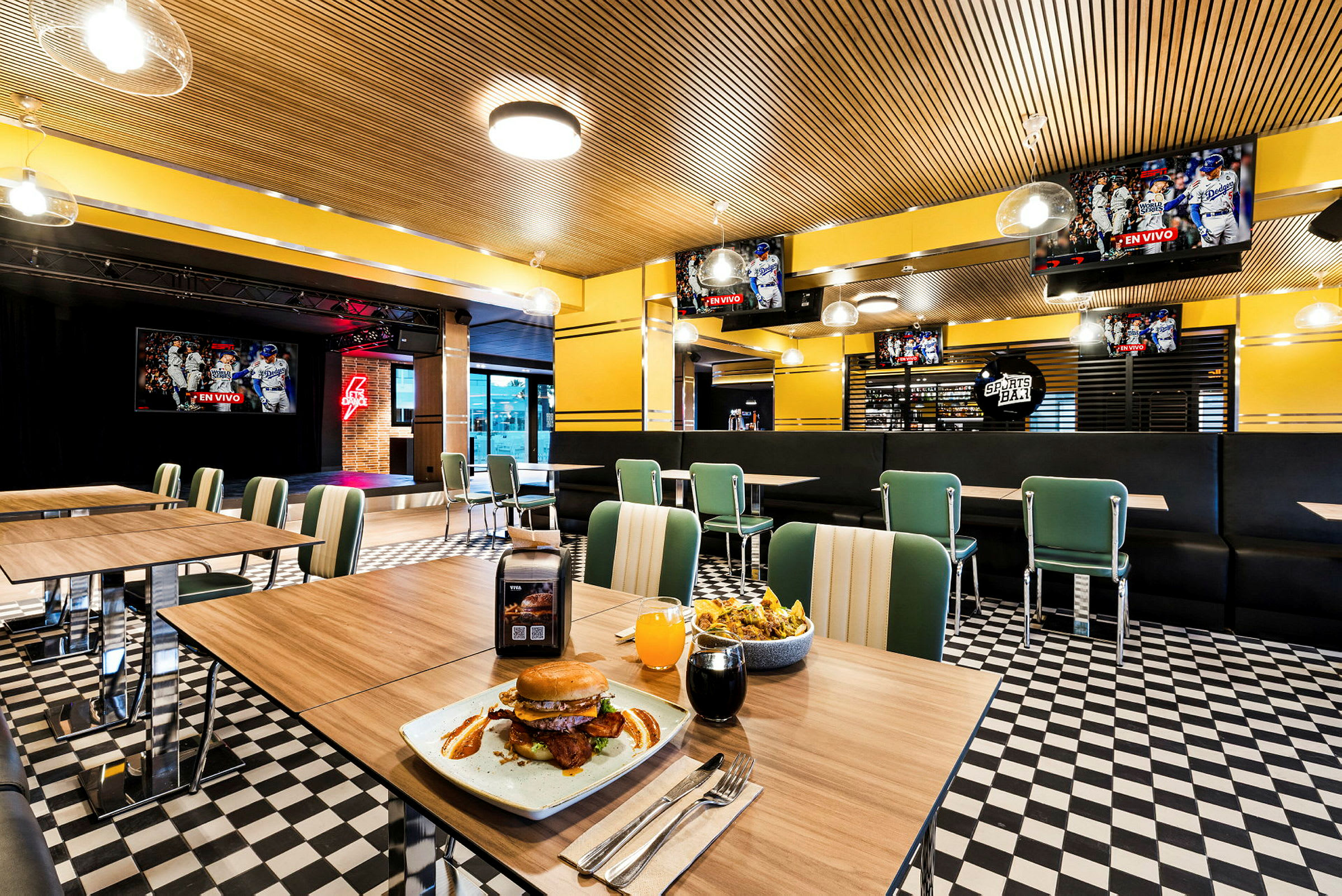 Interiör av en restaurang med bord och stolar, en tallrik med hamburgare och dryck på ett bord i förgrunden. (AI-genererad text)