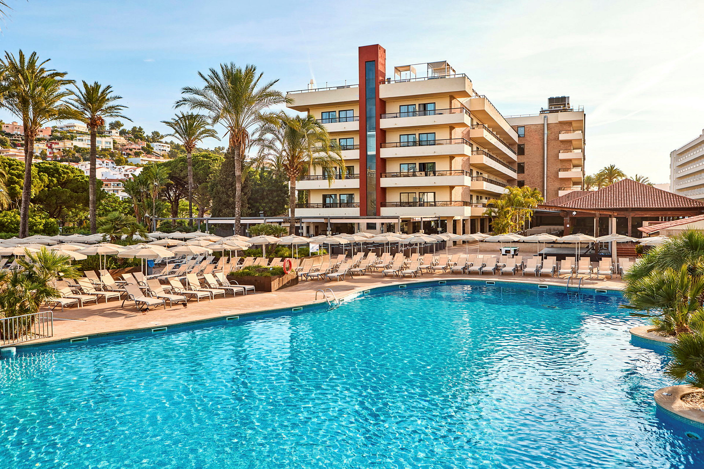 Bild av en hotellbyggnad omgiven av palmer, med en swimmingpool och solstolar i förgrunden. (AI-genererad text)