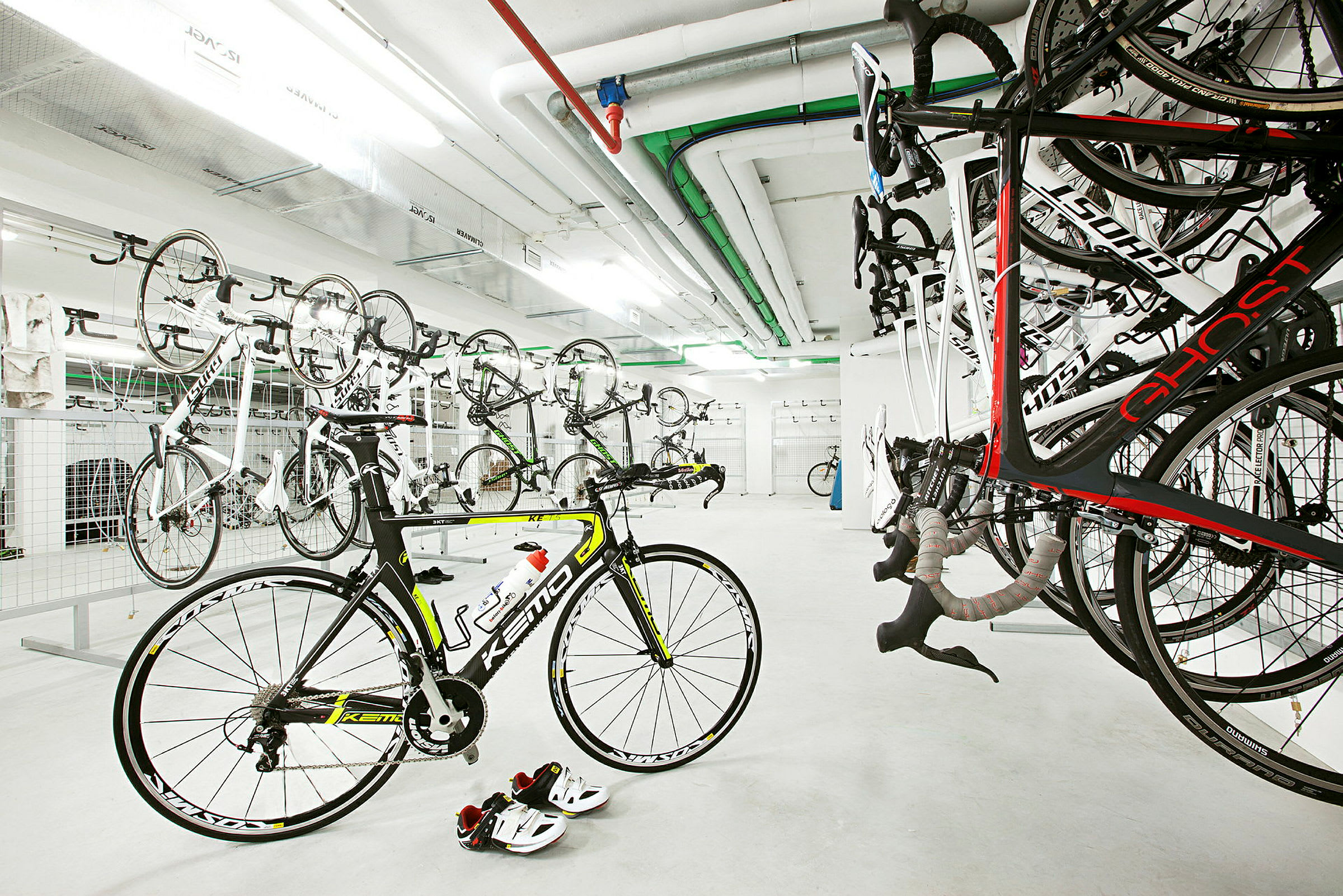 Ett cykelrum med flera cyklar upphängda på väggen och en cykel stående på golvet. (AI-genererad text)