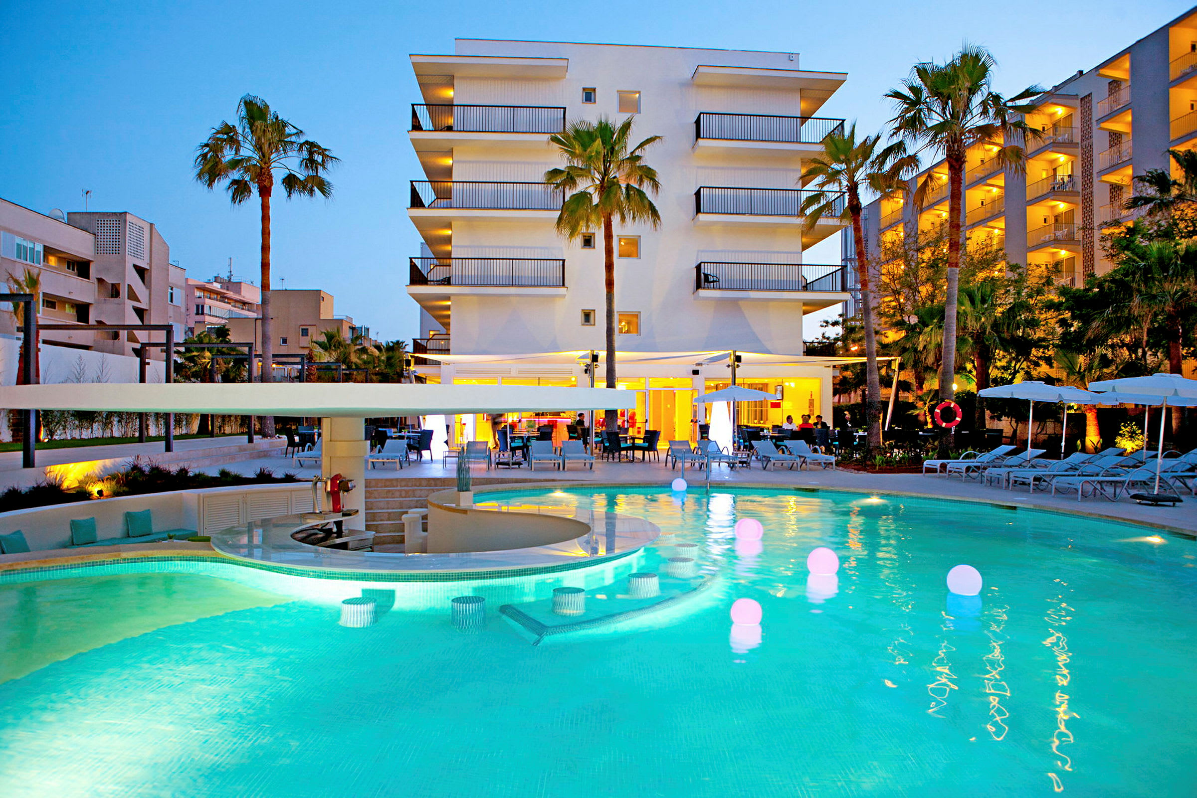 En hotellbyggnad med pool och solstolar framför på kvällen. (AI-genererad text)