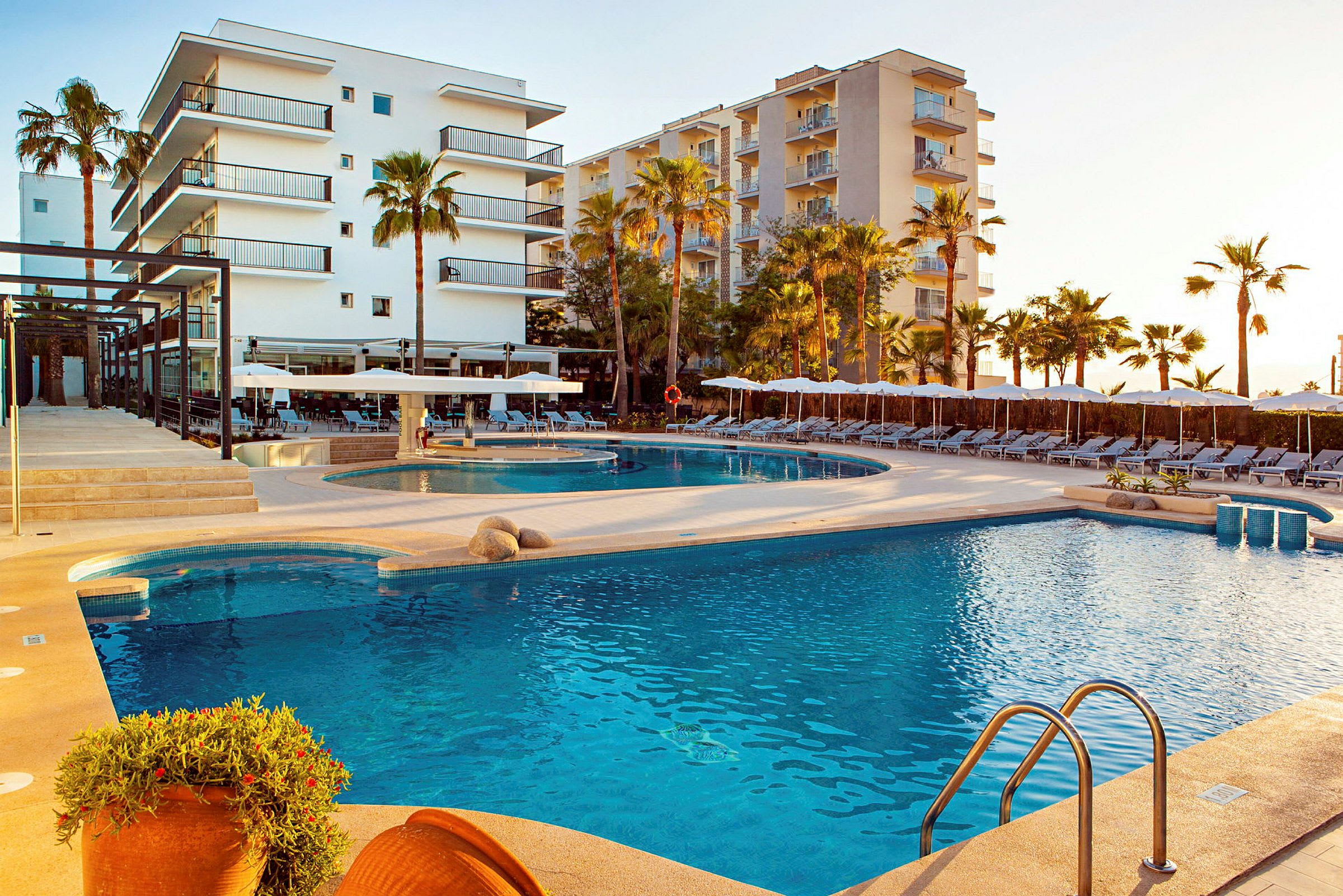 En utomhuspool med solstolar och palmer vid en hotellbyggnad. (AI-genererad text)