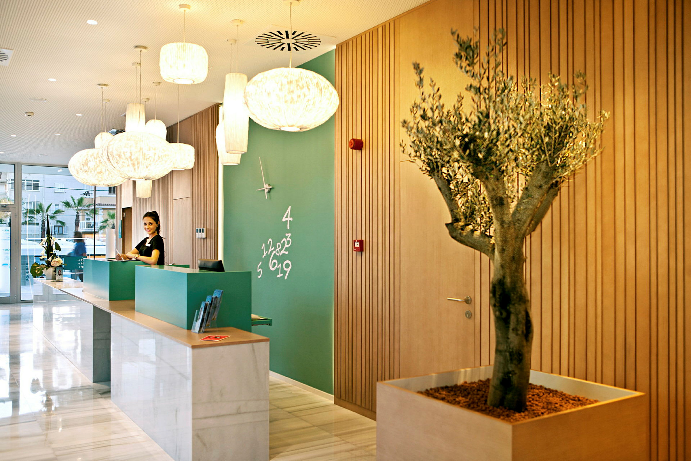 Reception av ett hotell med modern inredning, grön vägg med en klocka och numerisk dekoration, samt en trädkruka. (AI-genererad text)