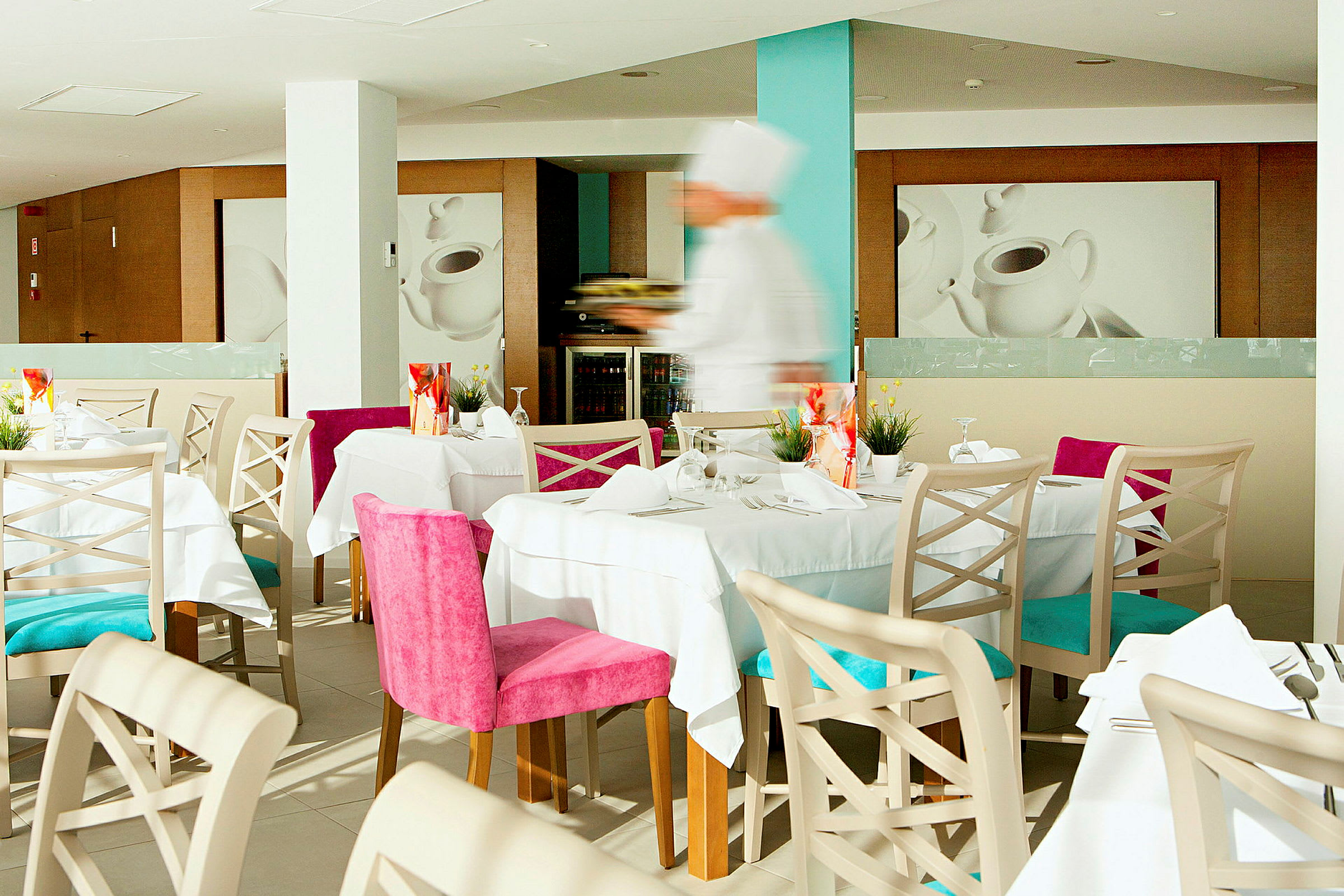 En restaurang med dukade bord, färgglada stolar och en suddig bild av en servitör i arbete. (AI-genererad text)