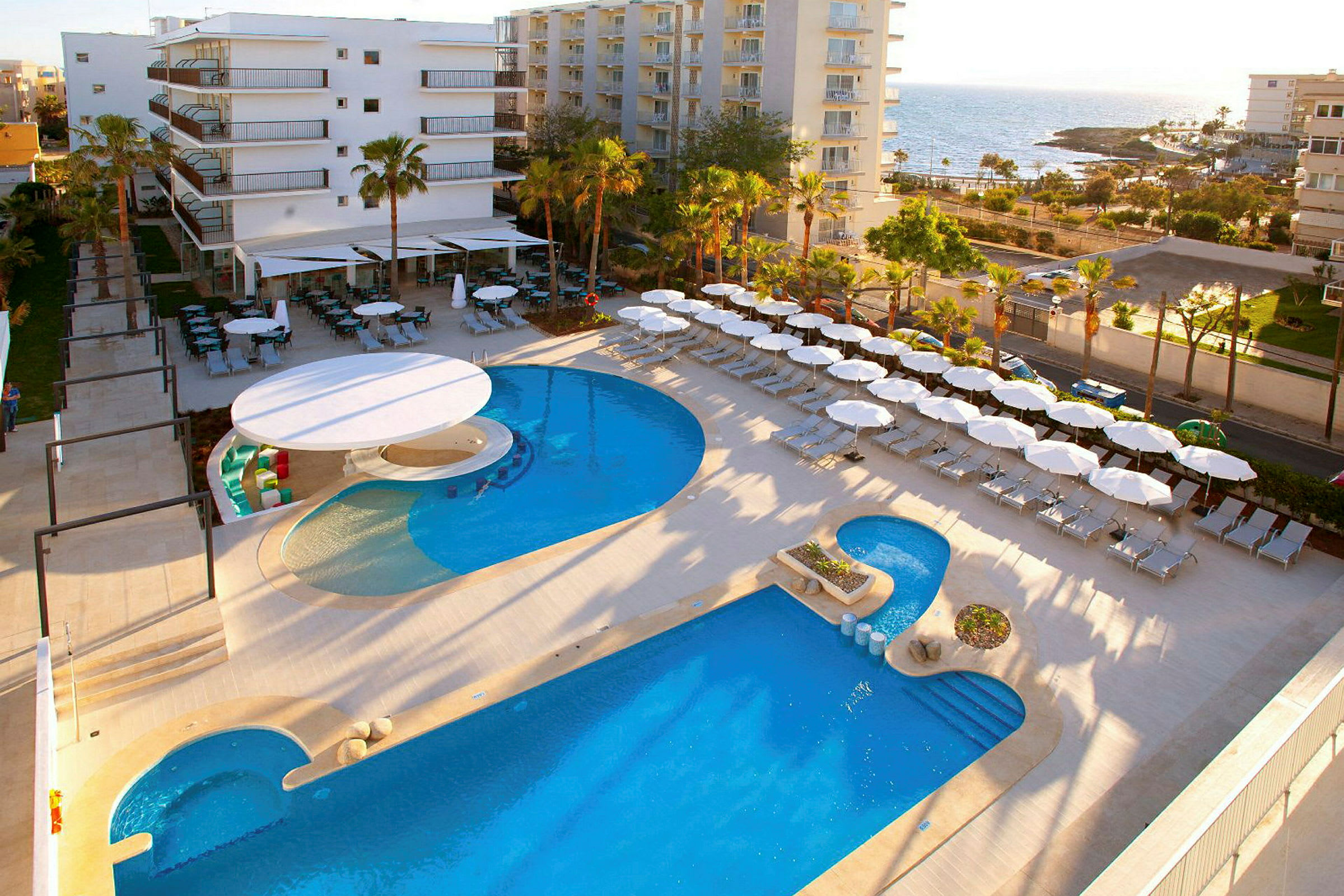 Hotellområde nära havet med pool, solstolar och parasoller. (AI-genererad text)