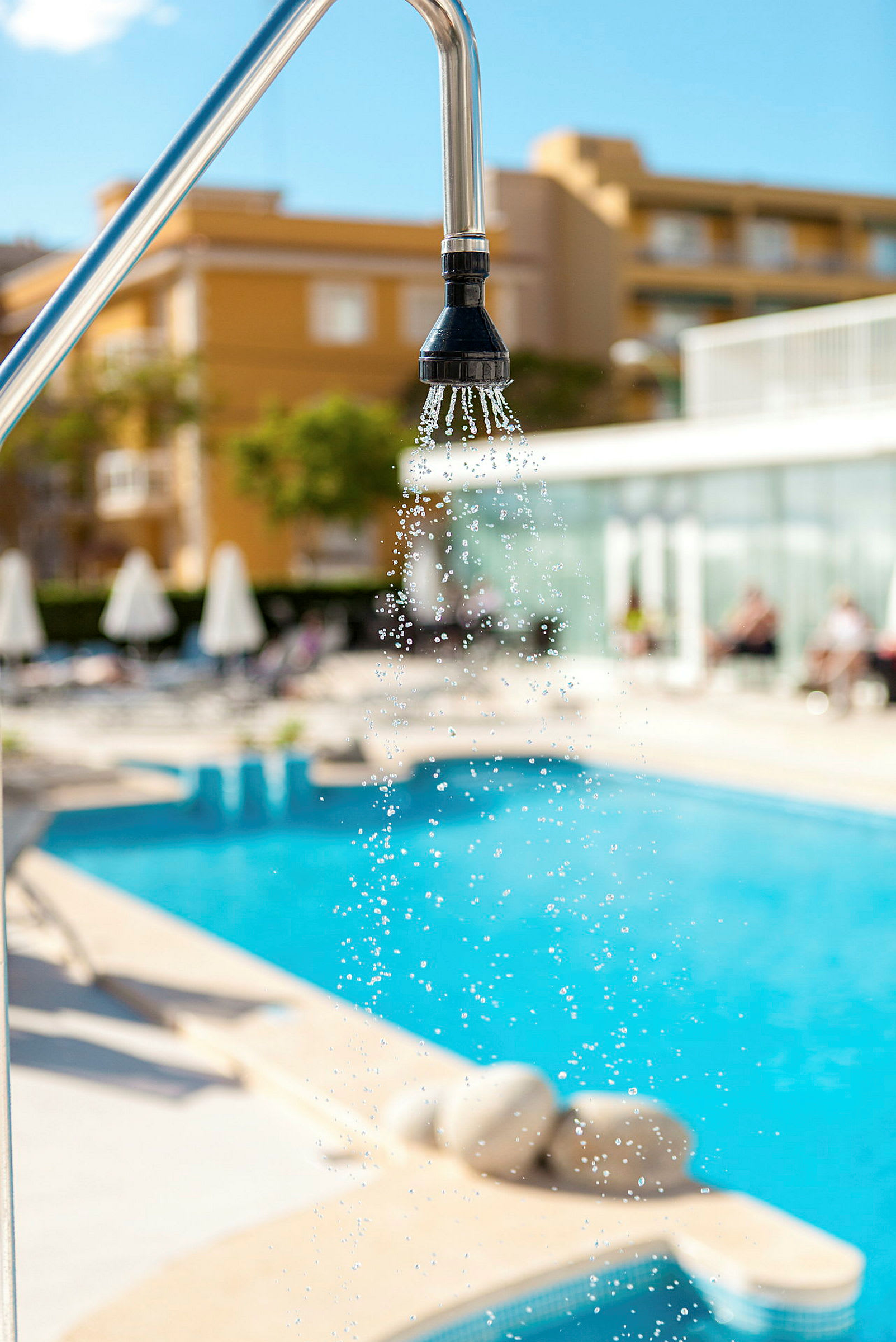 Duschen vid en pool, med parasoller och byggnad i bakgrunden. (AI-genererad text)