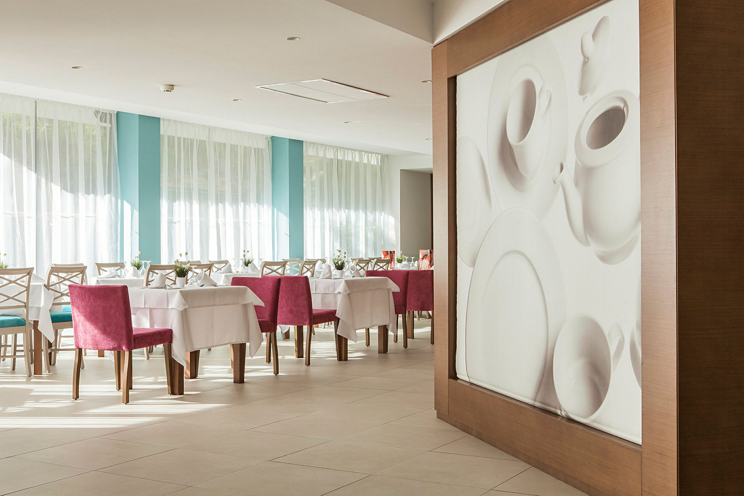Interiör av en restaurang med dukade bord och rosa stolar, samt en väggdekoration som foreställer porslin. (AI-genererad text)