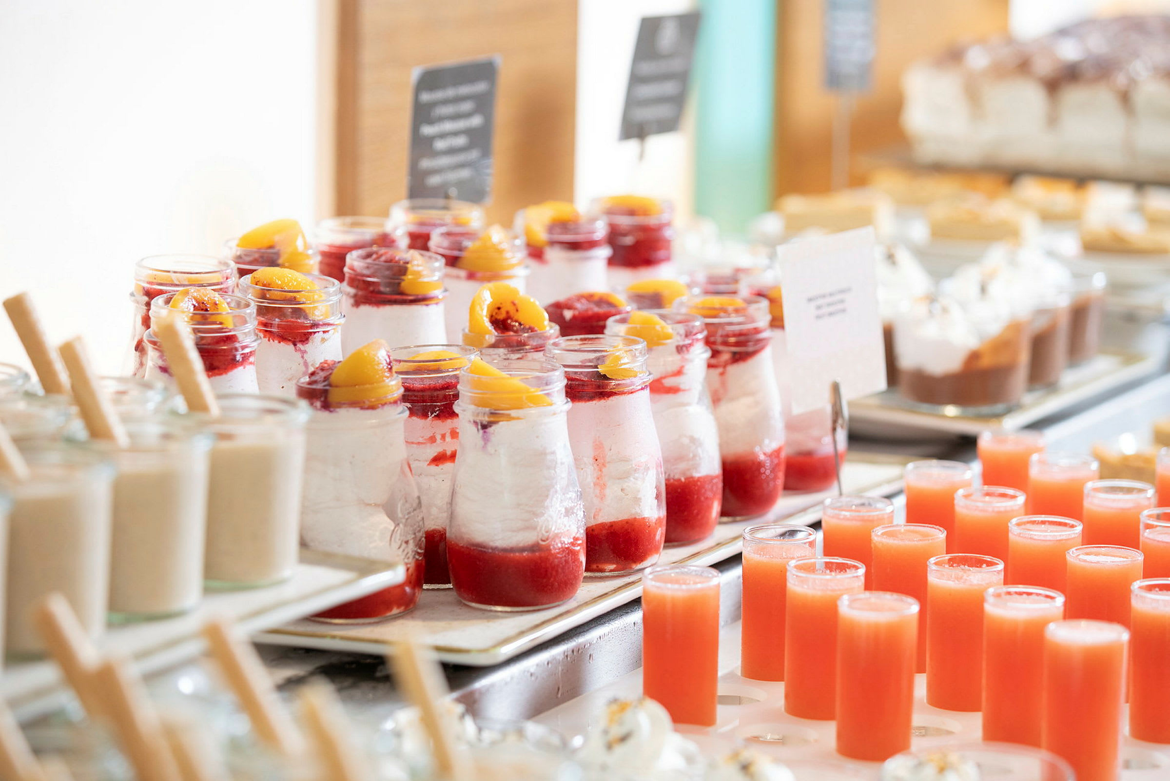 En rad av desserter i glas med röda fruktdetaljer och små juiceglas på ett bord. (AI-genererad text)