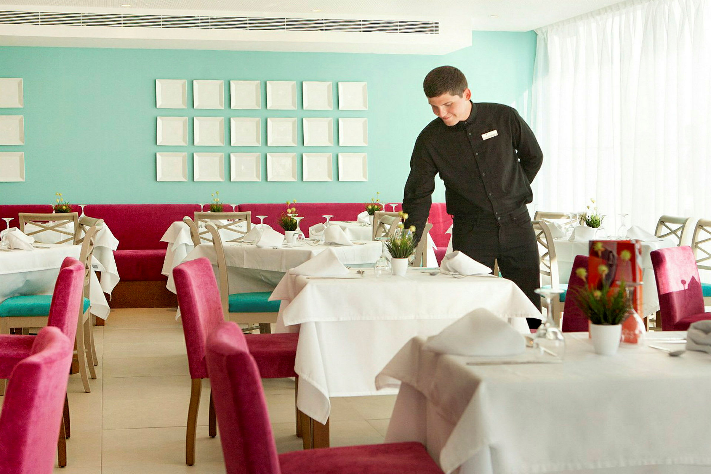 En elegant restaurang med dukade bord och färgglada stolar, en serveringspersonal förbereder ett bord. (AI-genererad text)