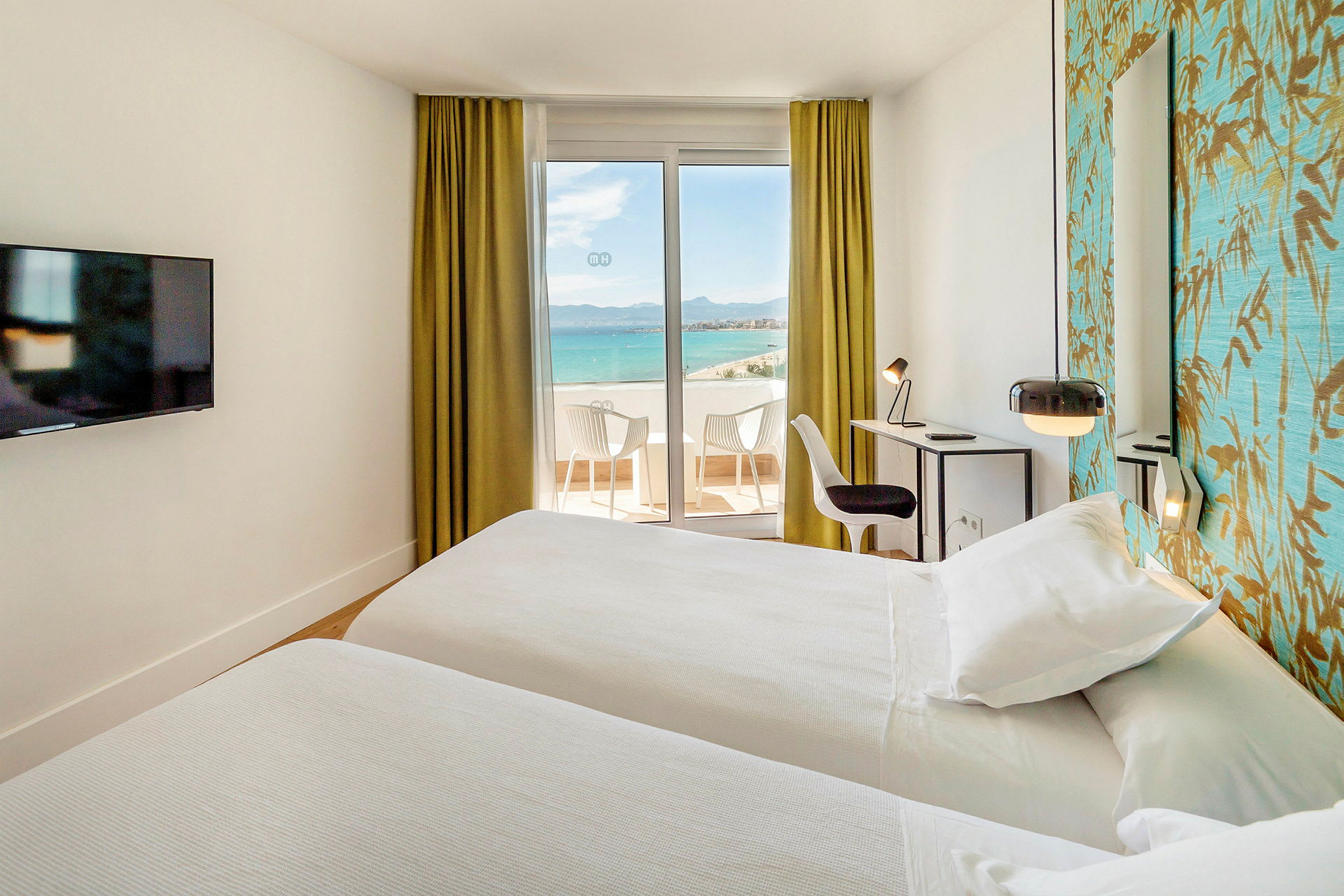 Hotellrum med havsutsikt, två sängar, skrivbord och en sittgrupp på balkongen. (AI-genererad text)