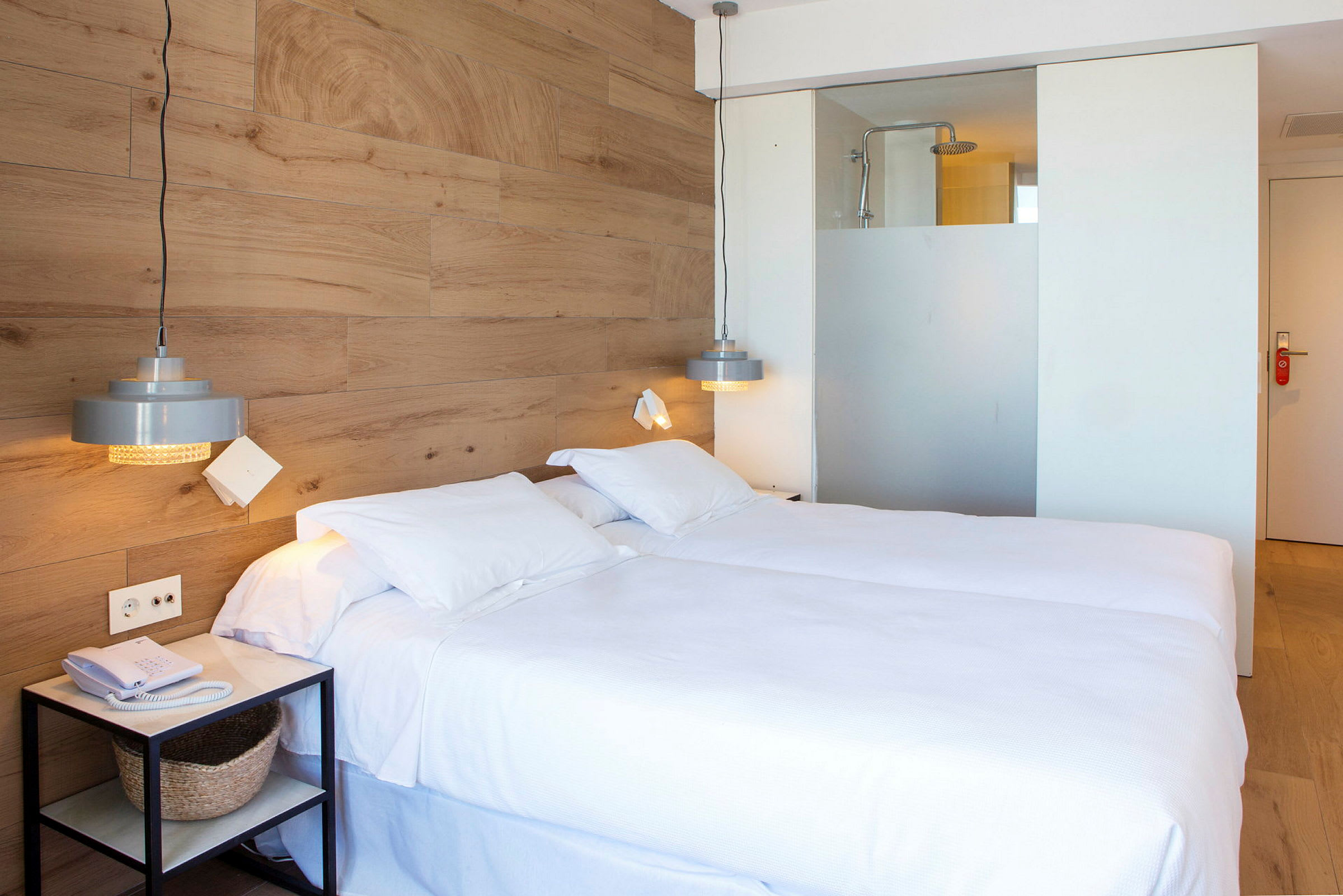 Hotellrum med en dubbelsäng, trävägg och en duschdel synlig bakom en glasvägg. (AI-genererad text)