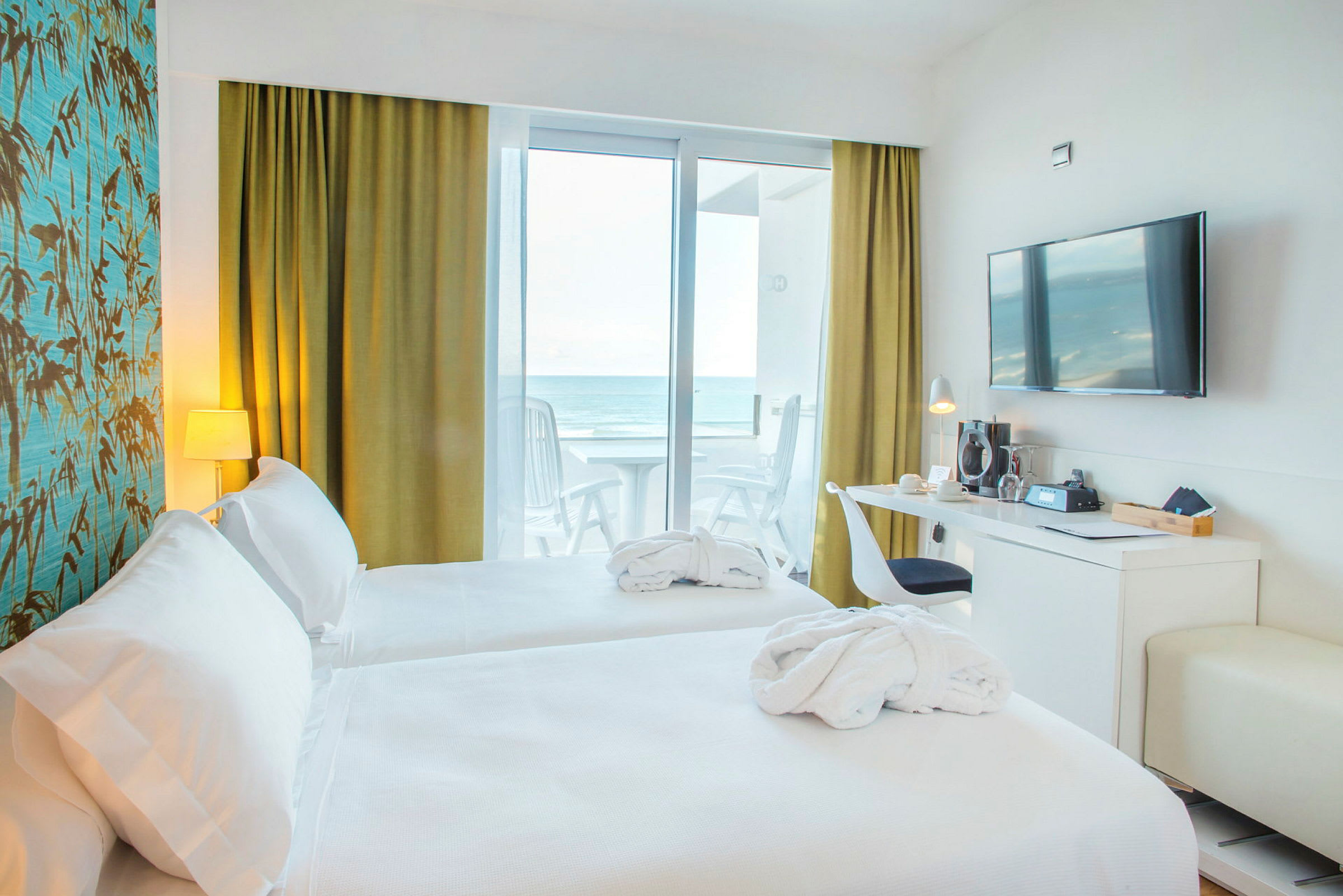 Hotellrum med två bäddar, skrivbord, vägg-TV och utsikt mot havet från balkong. (AI-genererad text)