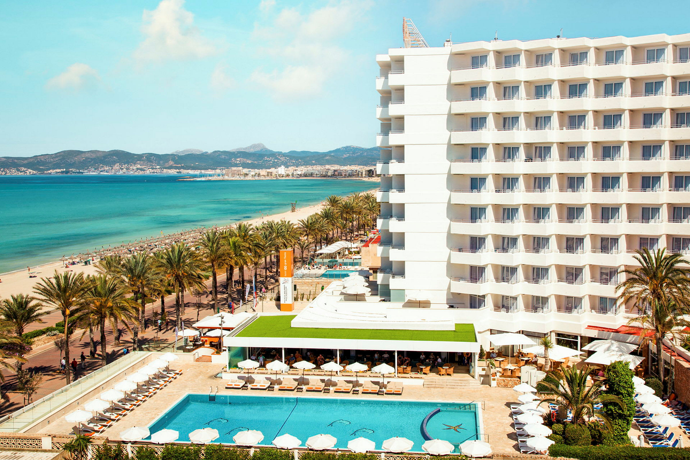 Hotell vid stranden med pool och solstolar, hav i bakgrunden. (AI-genererad text)