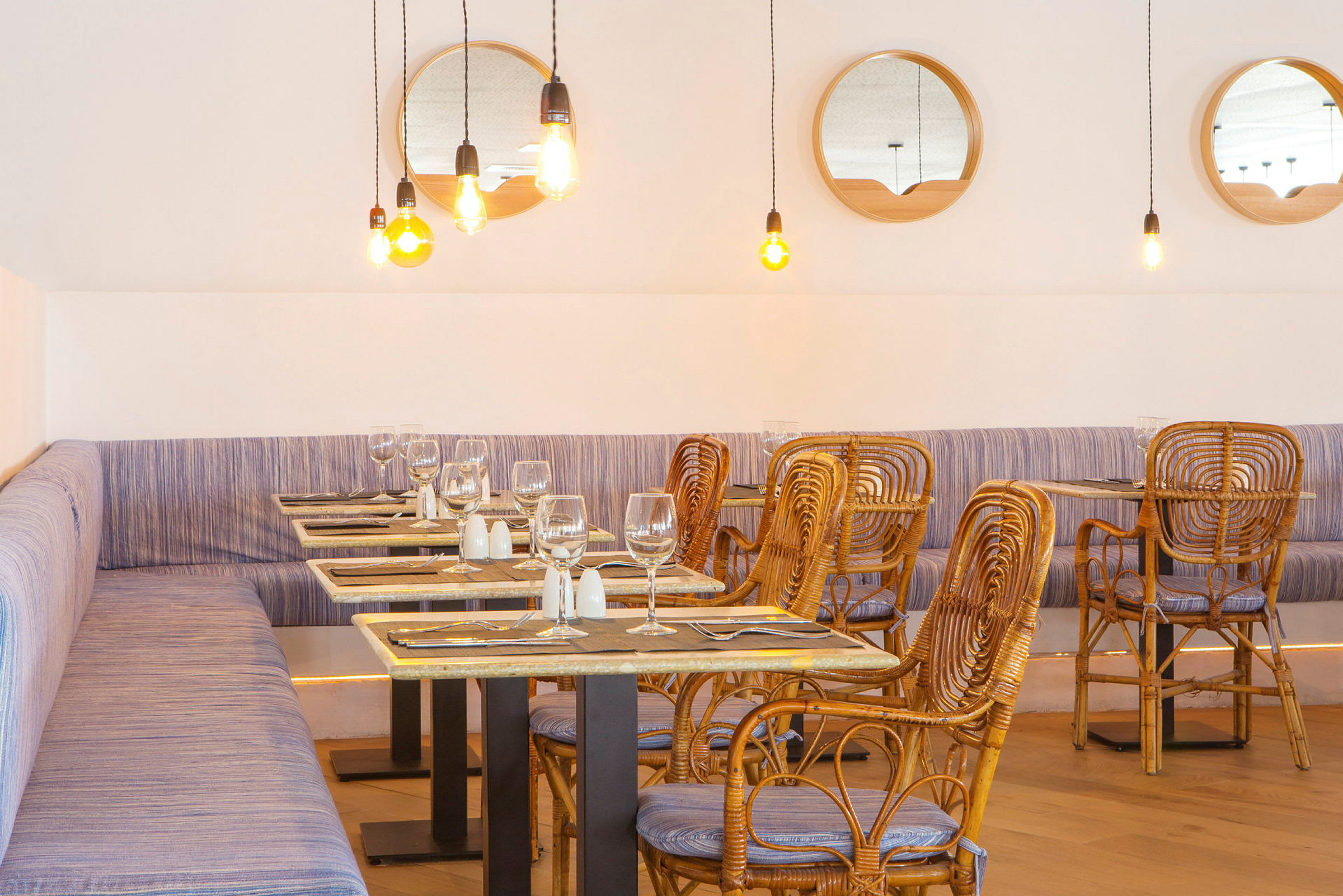 Restaurang med rottingstolar och bord, ljusa hängande lampor och speglar på väggen. (AI-genererad text)