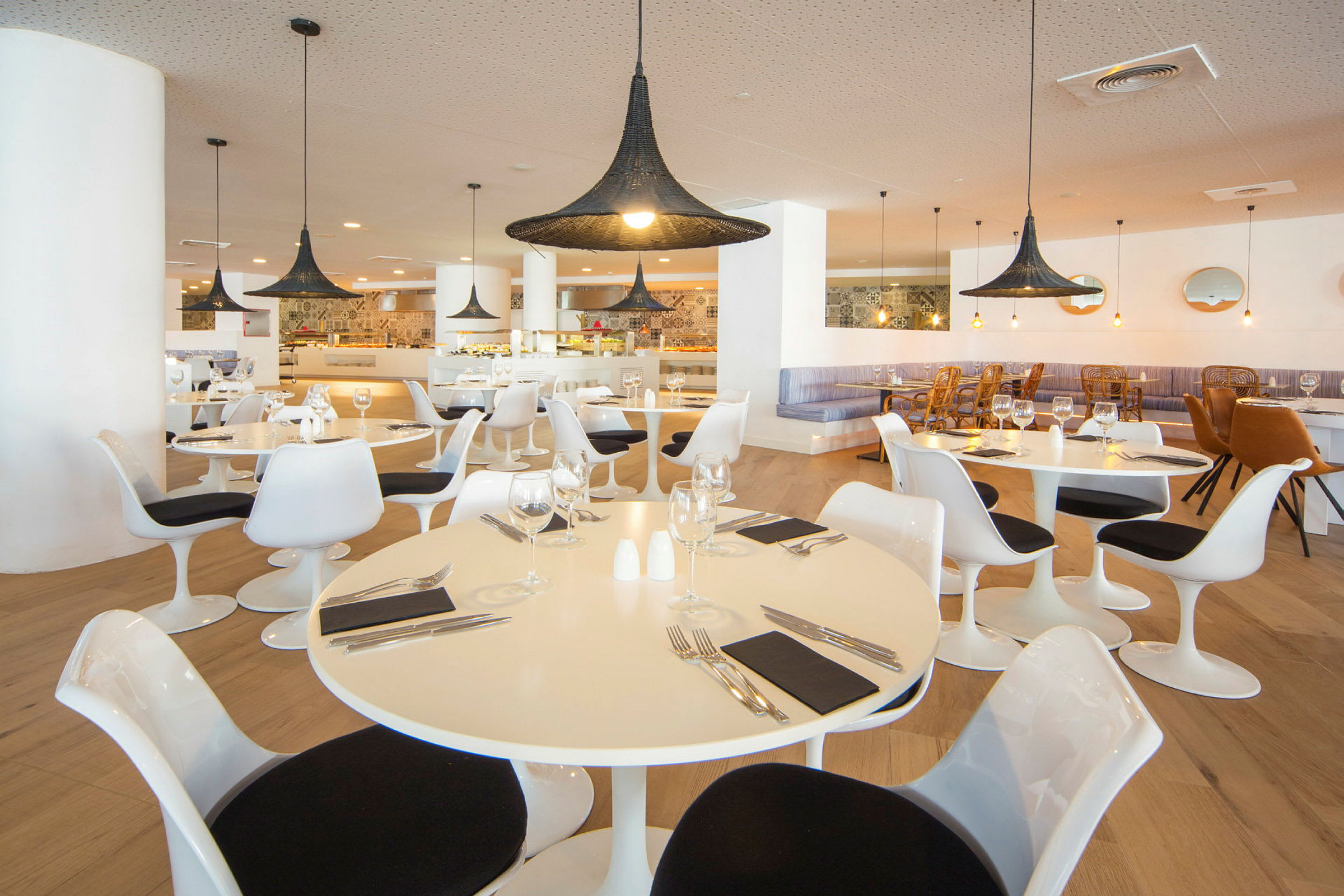 Bild på en restaurang med moderna vita bord och stolar, samt stora svarta lampor. (AI-genererad text)