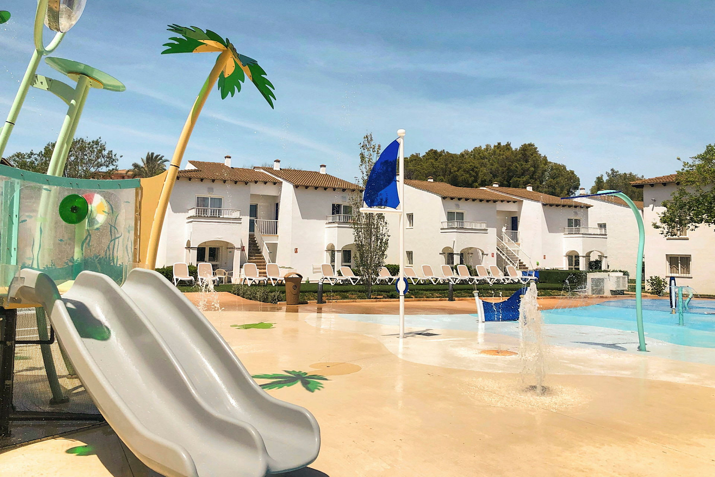 Barnpool med solsängar i bakgrunden vid hotell. (AI-genererad text)