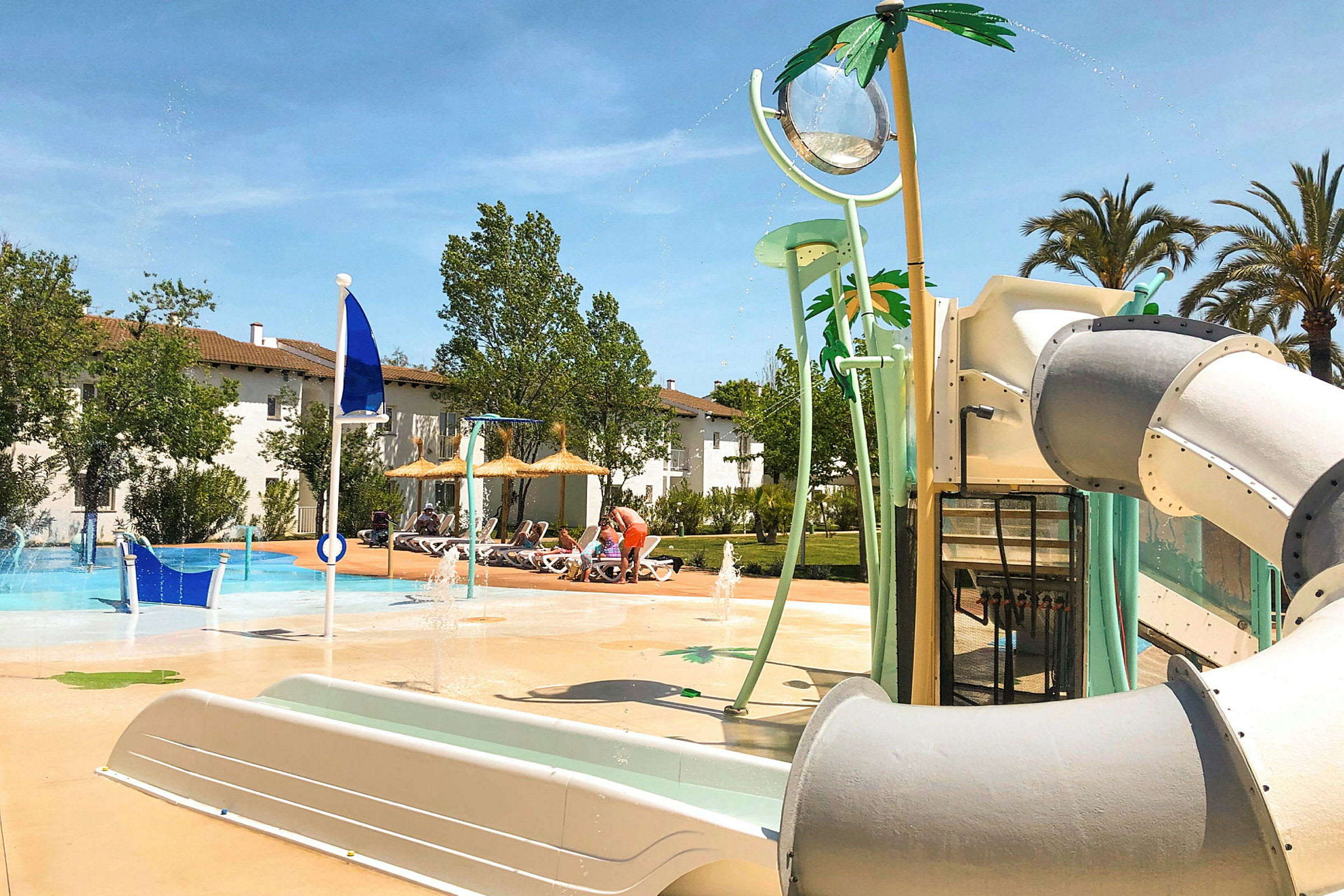 Bilden visar en pool med vattenleksaker och personer som njuter av aktiviteter under skuggtak. (AI-genererad text)